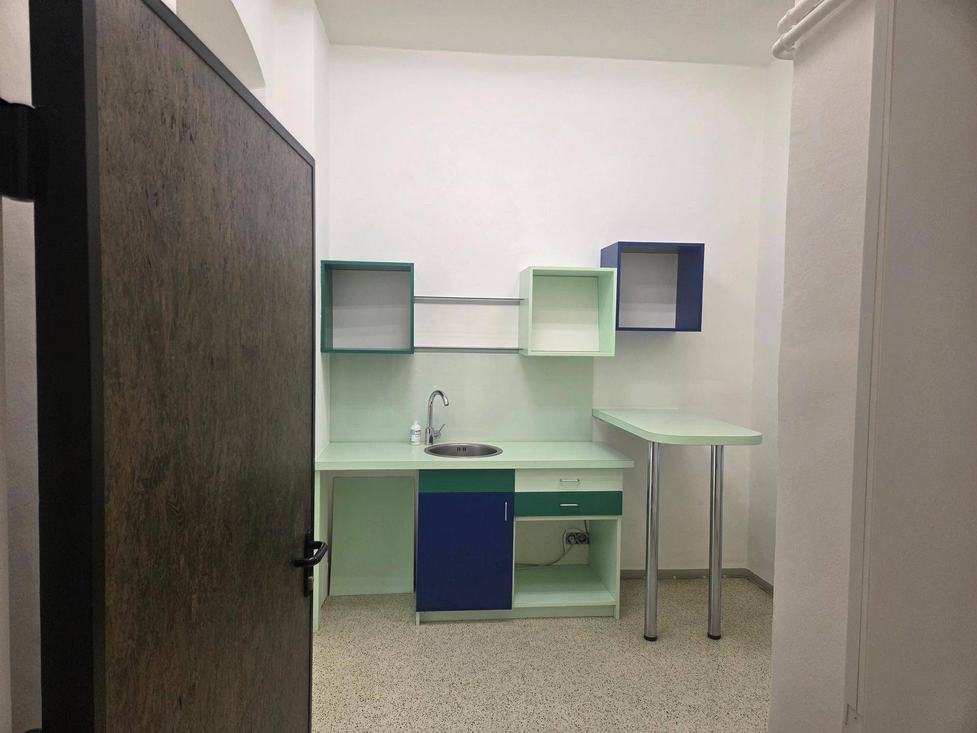 Kleine Küchenzeile mit Spüle, blauen und grünen Schränken und einer Arbeitsplatte.