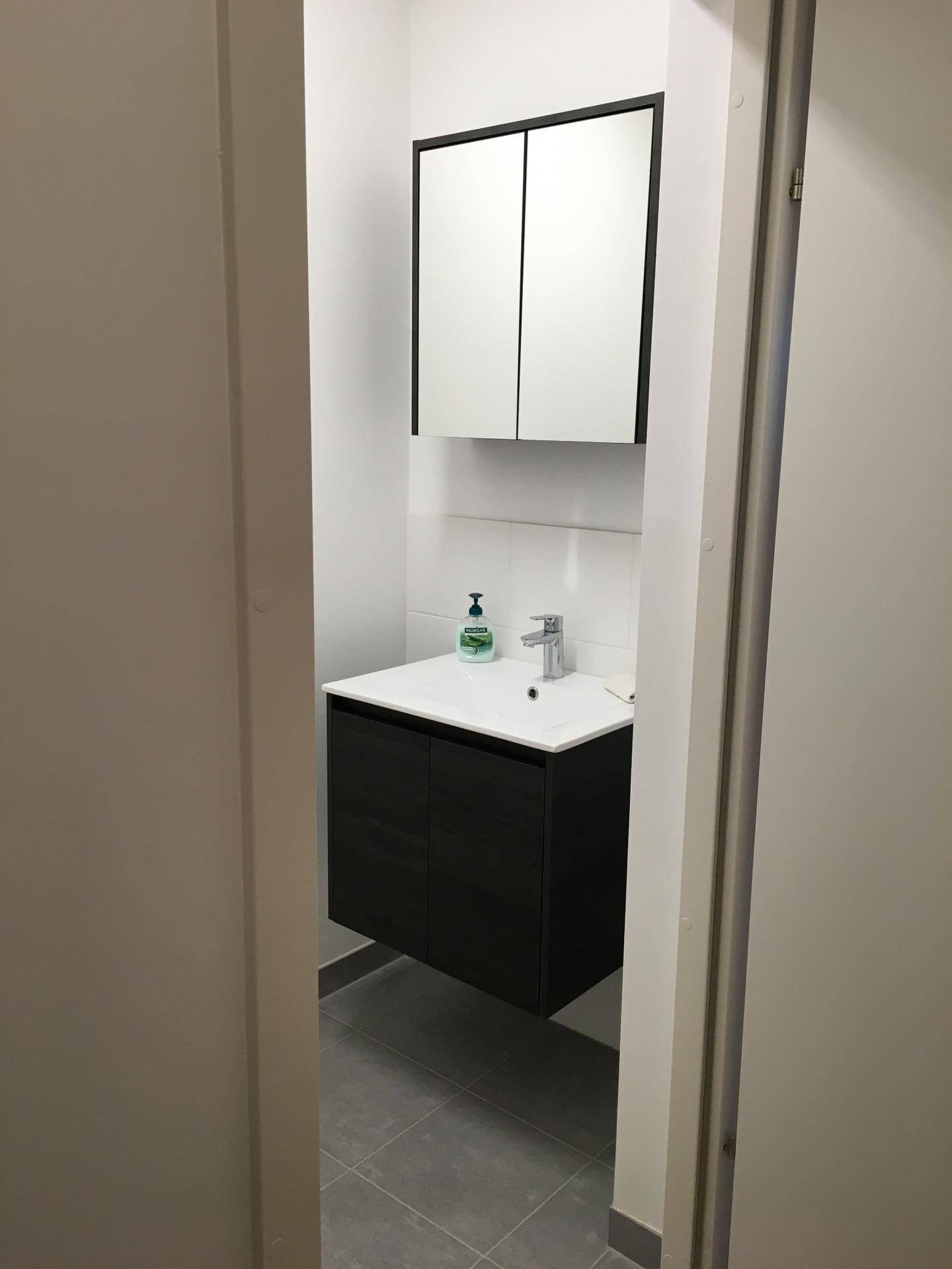 Kleines Gäste-WC mit modernem Waschtisch, Spiegelschrank und grauen Fliesen.