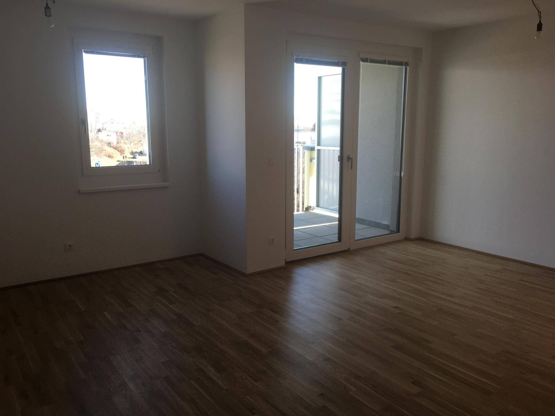 Lichtdurchfluteter Raum mit Laminatboden und großem Balkonzugang, ideal für Wohnzwecke.