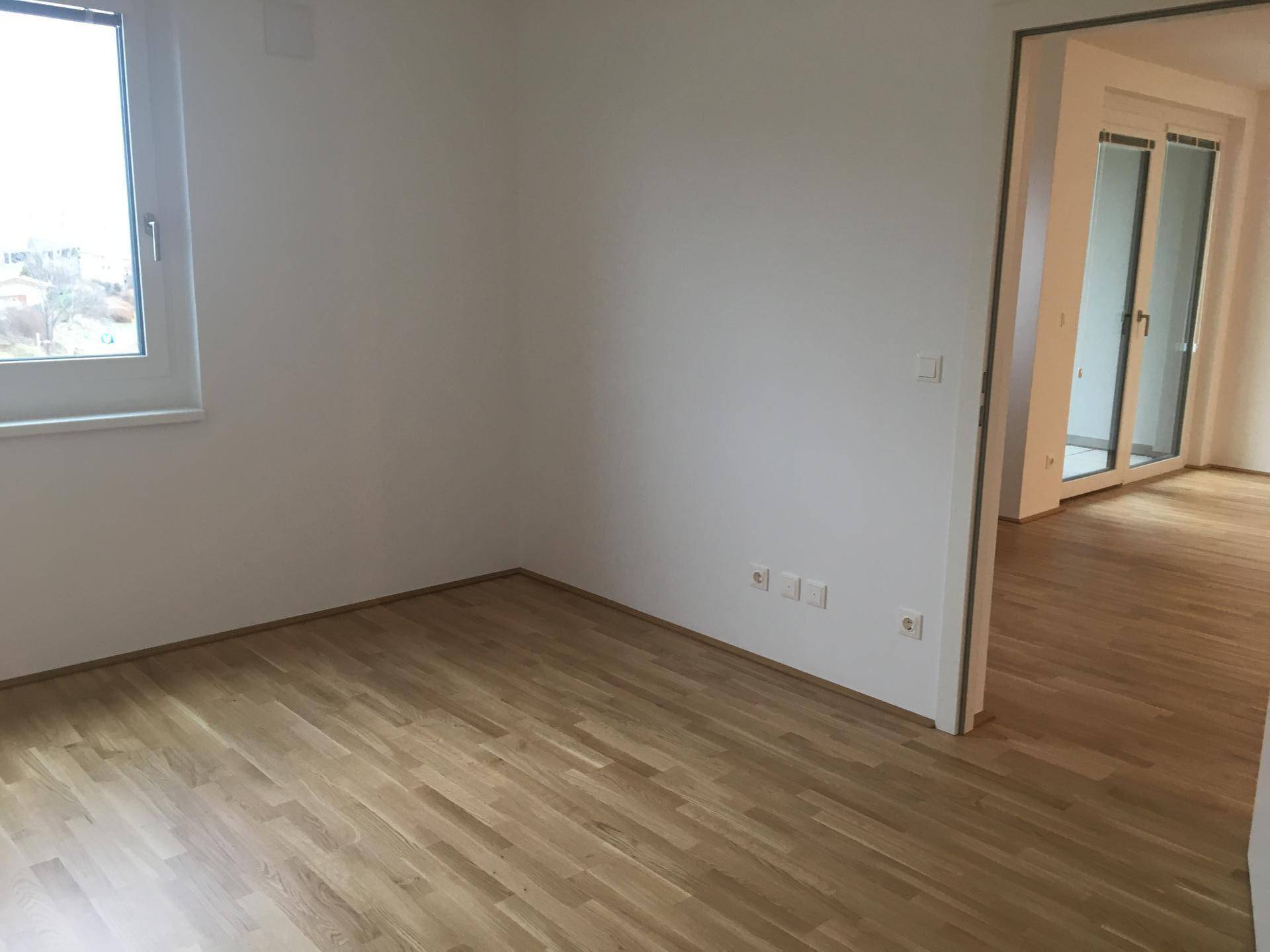 Heller, leerer Raum mit Laminatboden und einem Fenster, bereit zur individuellen Gestaltung.