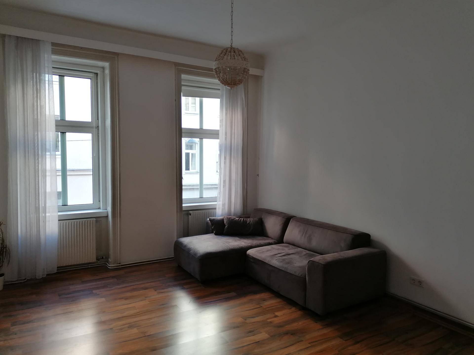 Gemütliches Wohnzimmer mit braunem Sofa, großen Fenstern und Laminatboden.