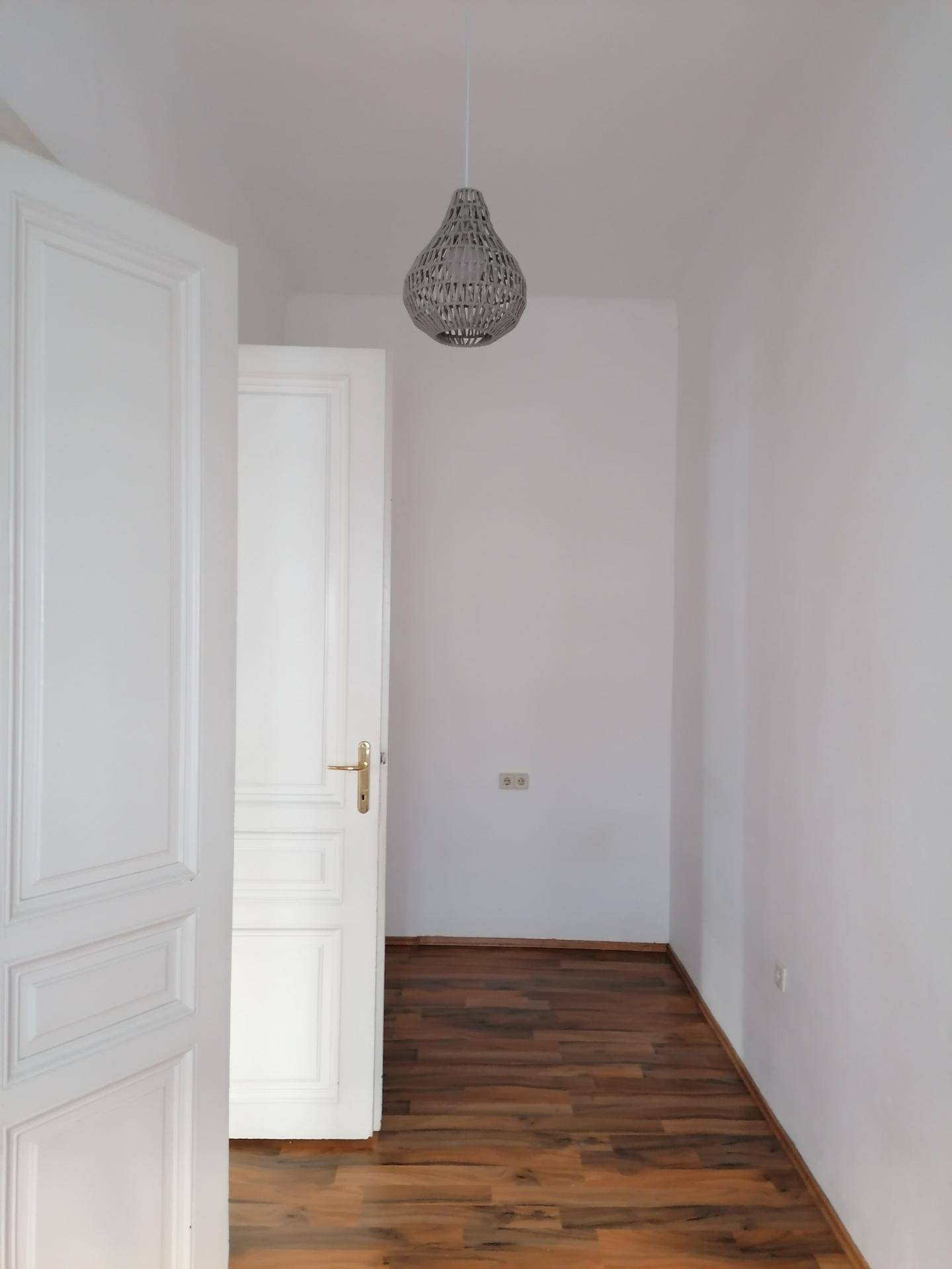 Heller Flur mit weißer Tür, Laminatboden und moderner Hängelampe.