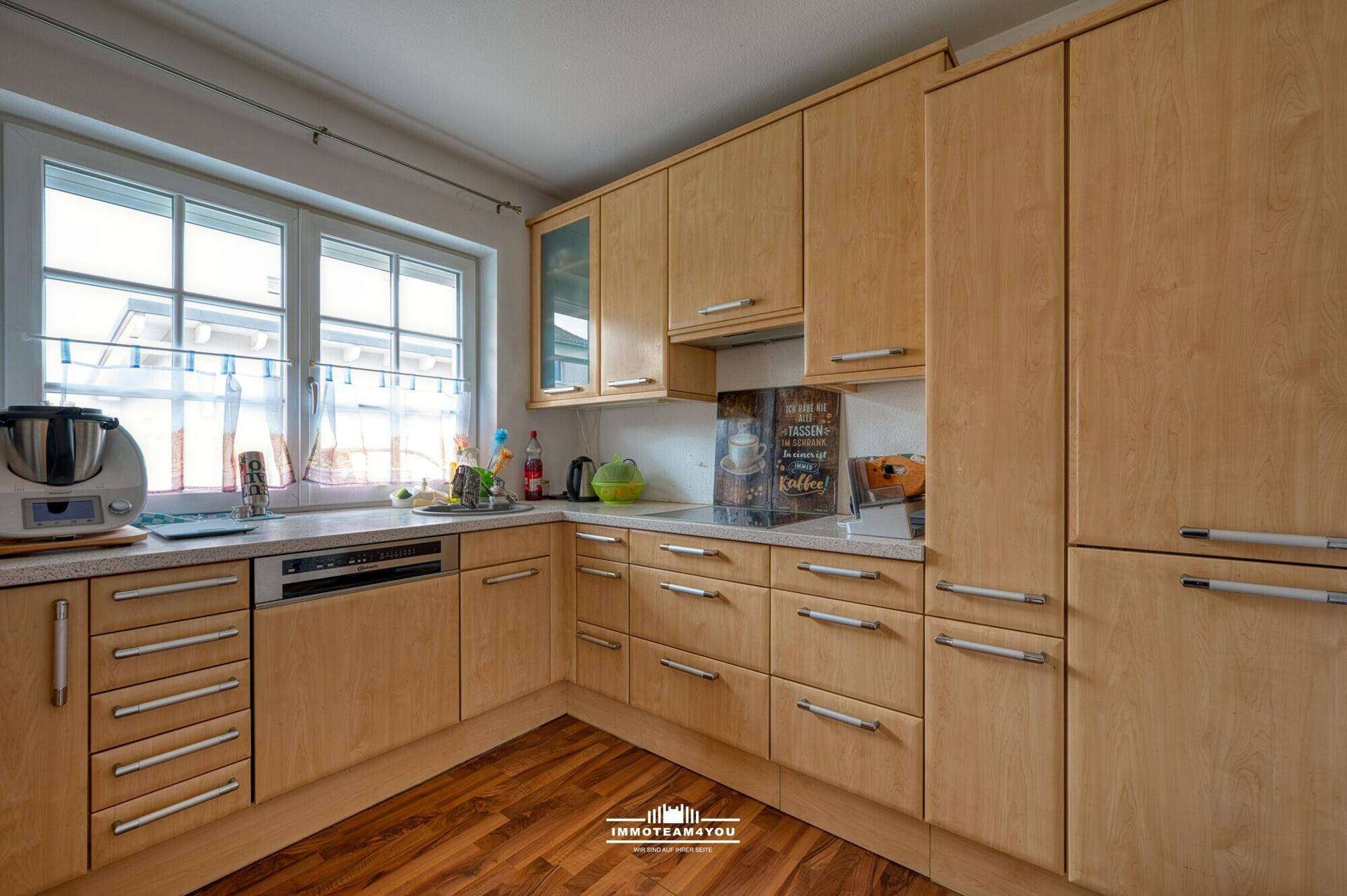 Funktionale Küche mit hellen Holzschränken, Laminatboden und Fenster.