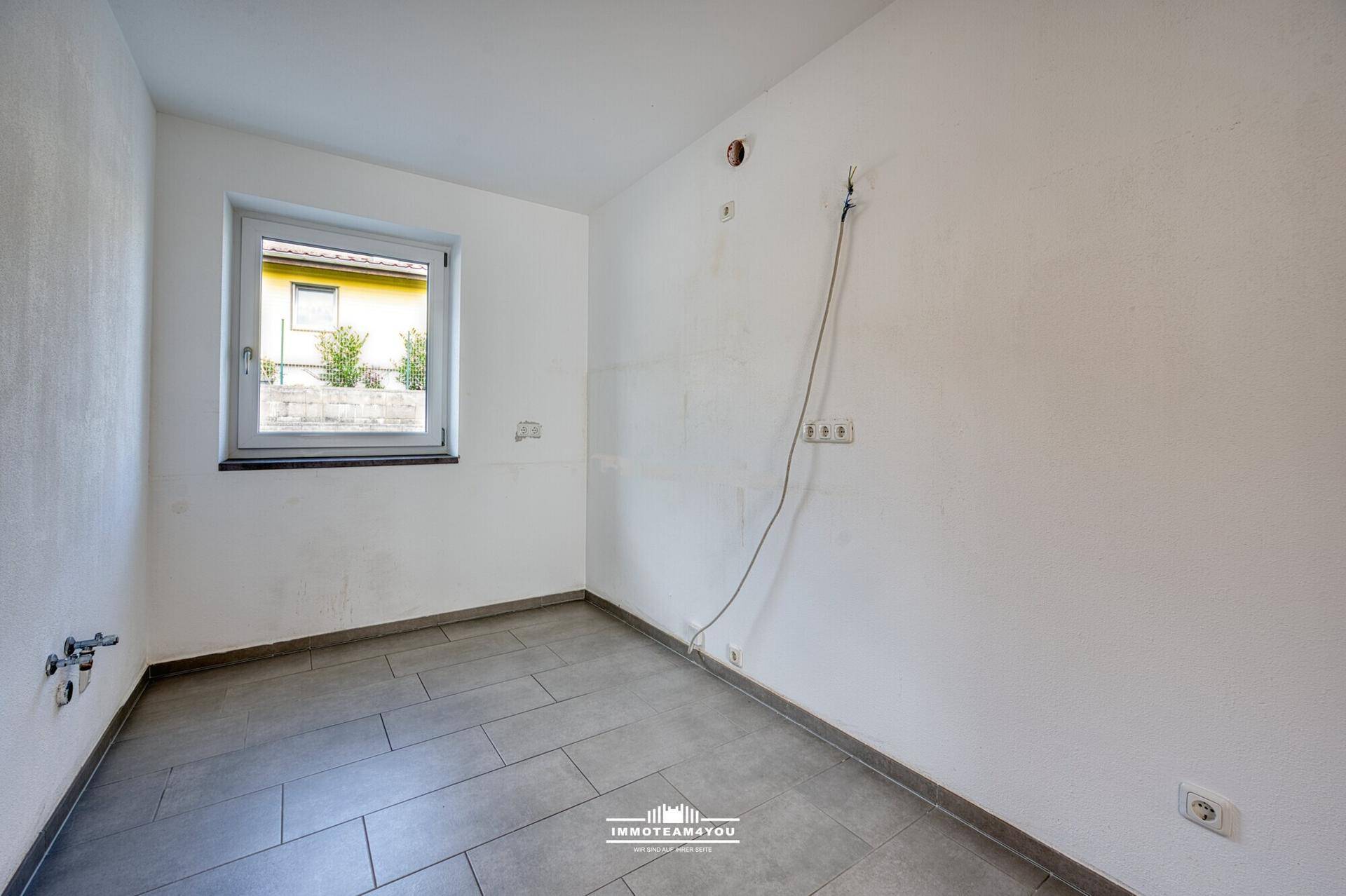 Leerer Raum mit Fliesenboden und sichtbaren Anschlüssen, ideal für eine Küche oder Waschküche.