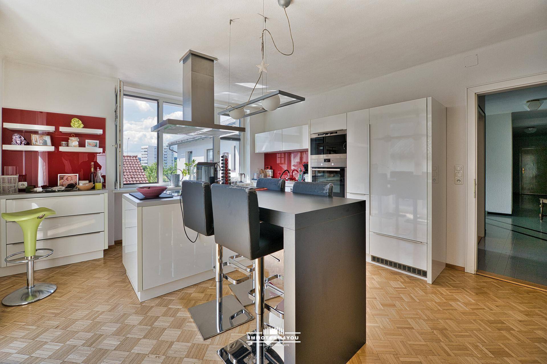 Moderne Küche mit Kochinsel, Hochglanzfronten und Parkettboden, offen zum Wohnbereich.