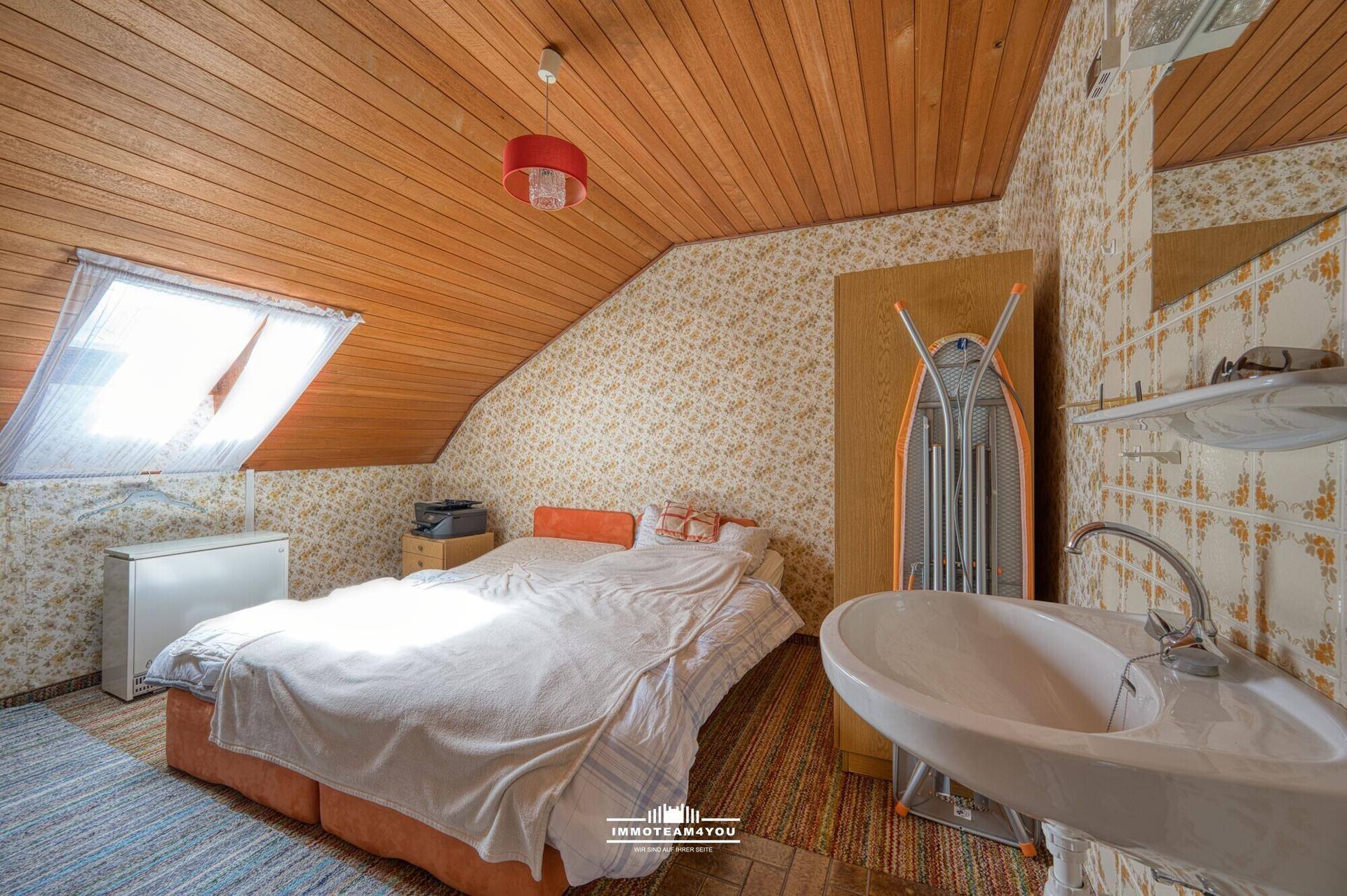 Dachgeschosszimmer mit Schräge, Dachfenster, Holzdecke und integriertem Waschbecken.