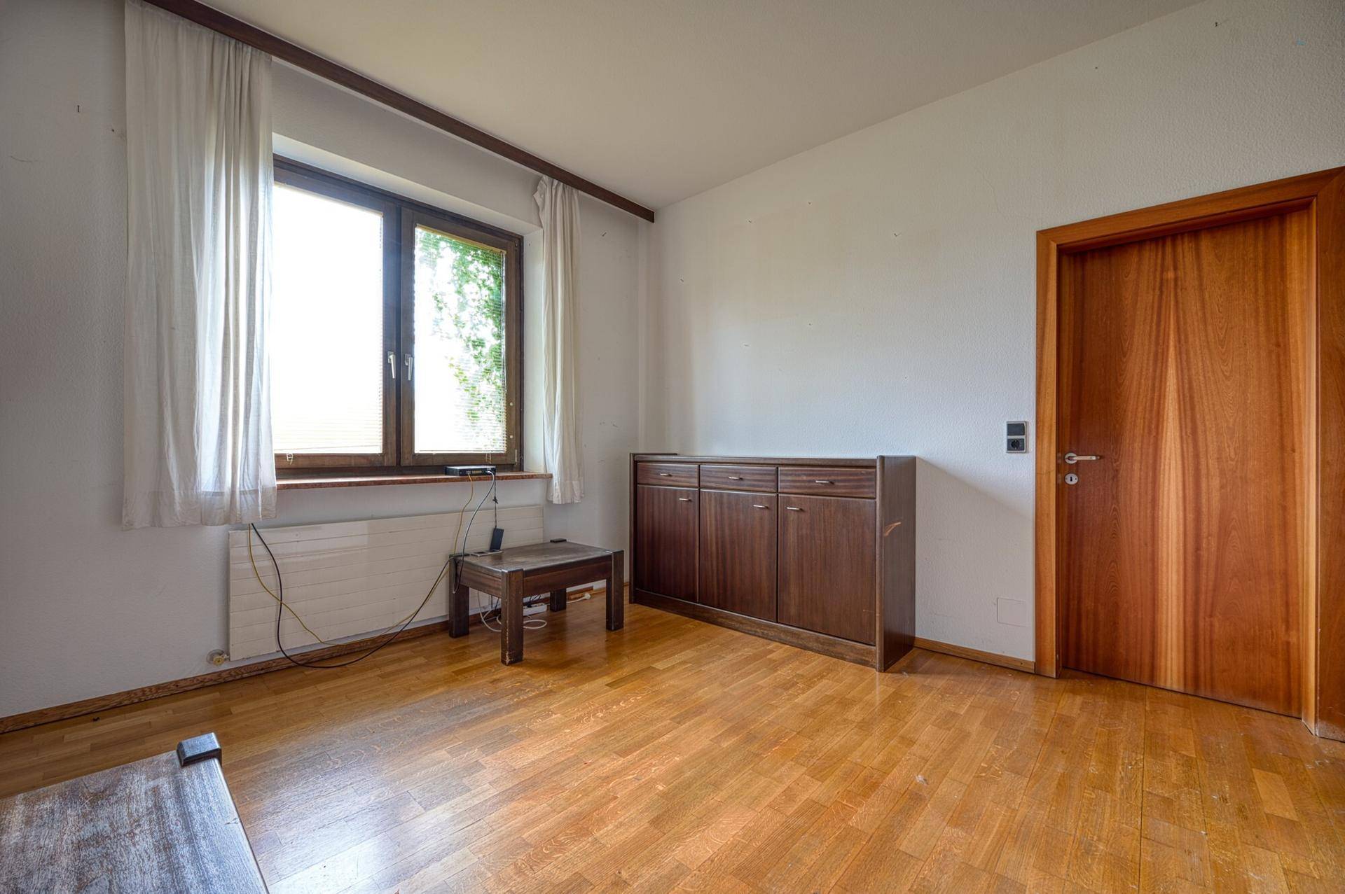 Helles Schlafzimmer mit Holzboden, großem Fenster und Holztür, bereit zur individuellen Gestaltung.