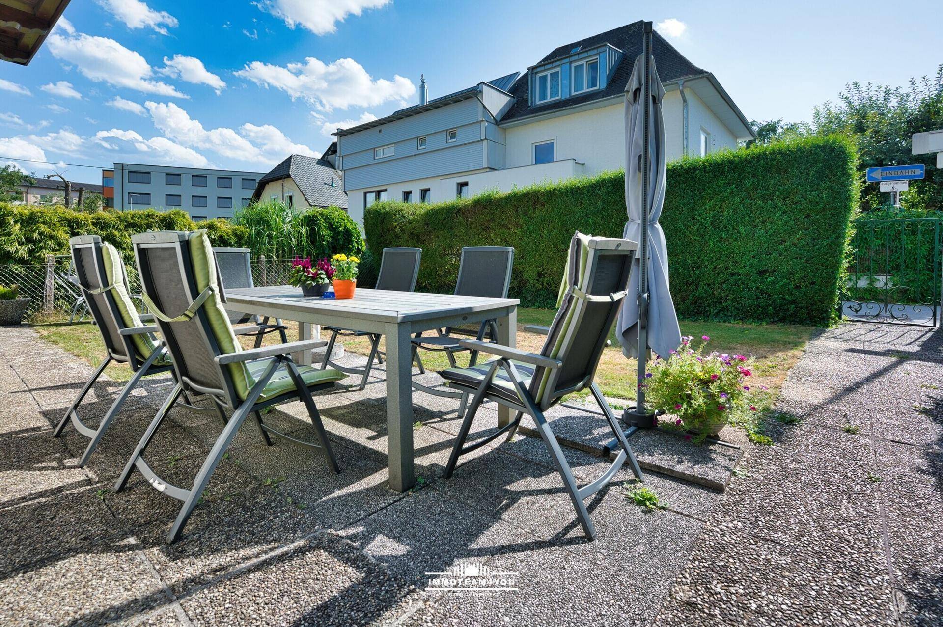 Geräumige Terrasse mit Esstisch und Stühlen, umgeben von einem gepflegten Garten und Hecken.