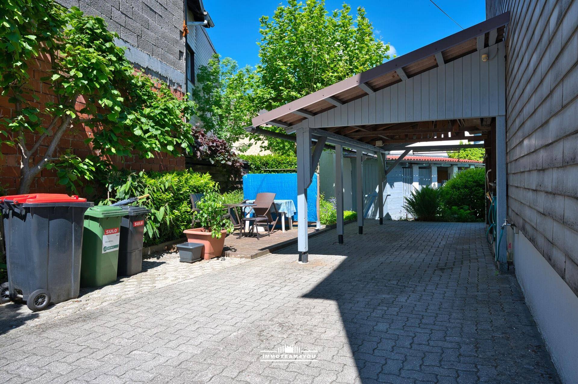 Gepflasterter Hofbereich mit überdachtem Carport und kleiner Sitzecke im Freien.
