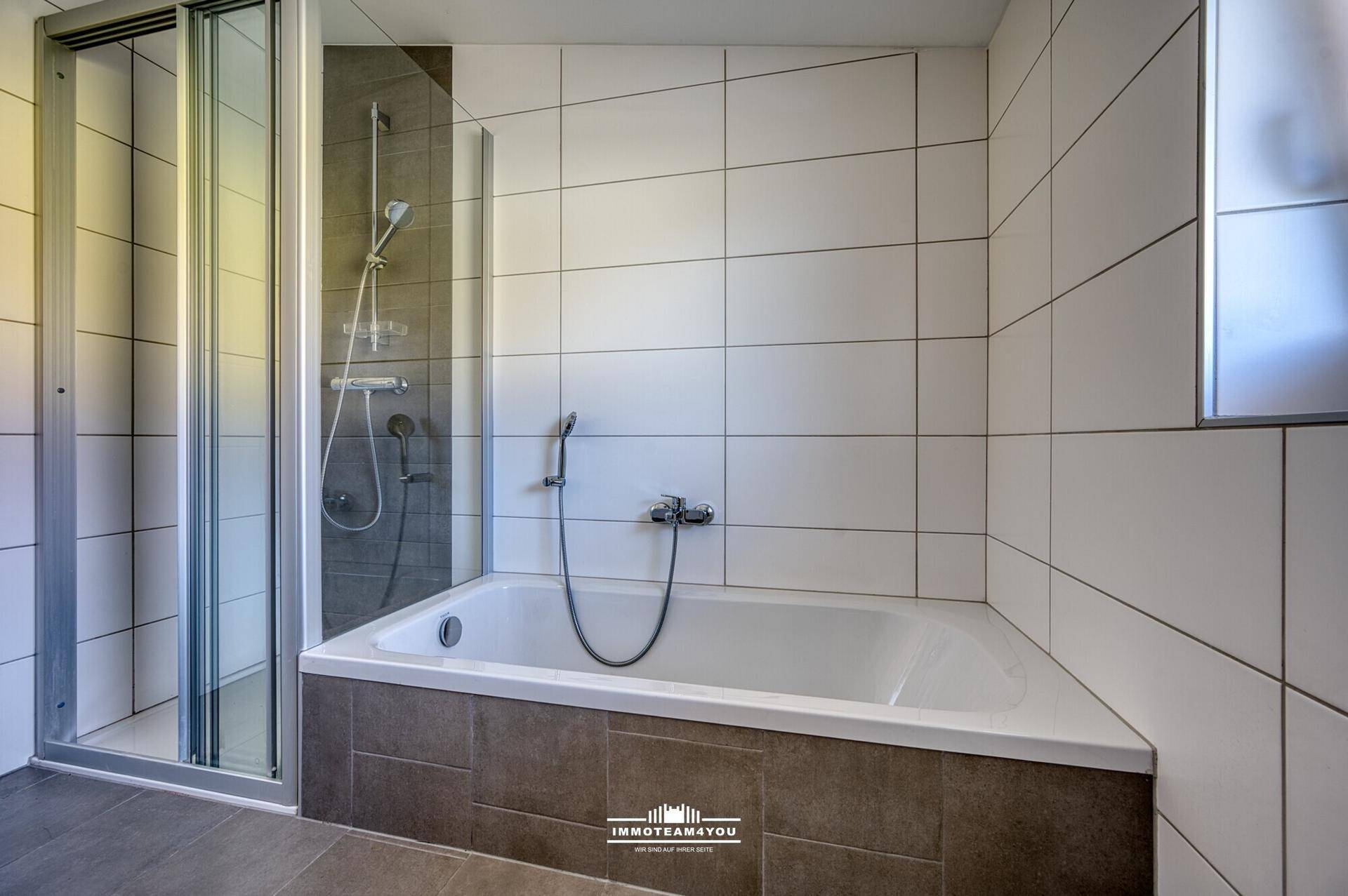Modernes Badezimmer mit Badewanne, Duschkabine und grauen Fliesen an Wänden und Boden.