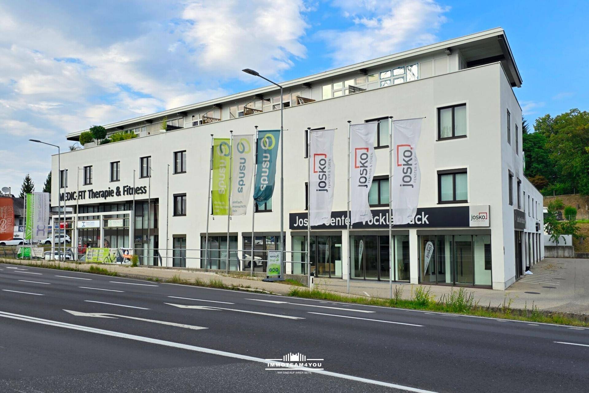 Modernes Geschäftsgebäude mit weißer Fassade, großen Fenstern und Werbeflaggen unter bewölktem Himmel.