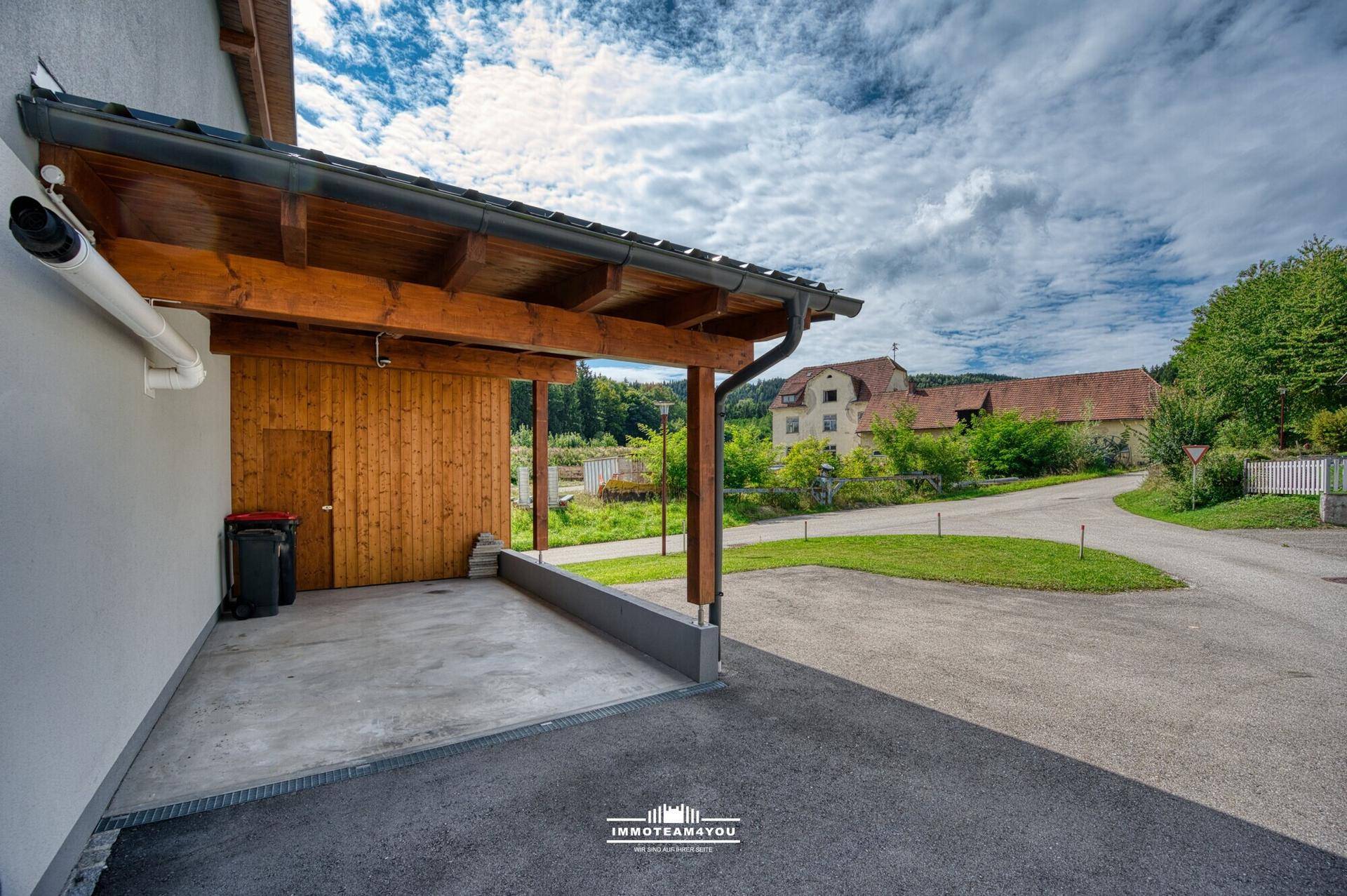 Überdachter Carport aus Holz mit Betonboden und direktem Zugang zum Grundstück.