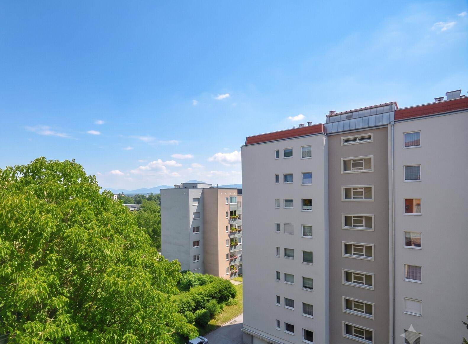 Mehrere Wohngebäude umgeben von grünen Bäumen mit Blick auf die entfernten Berge.
