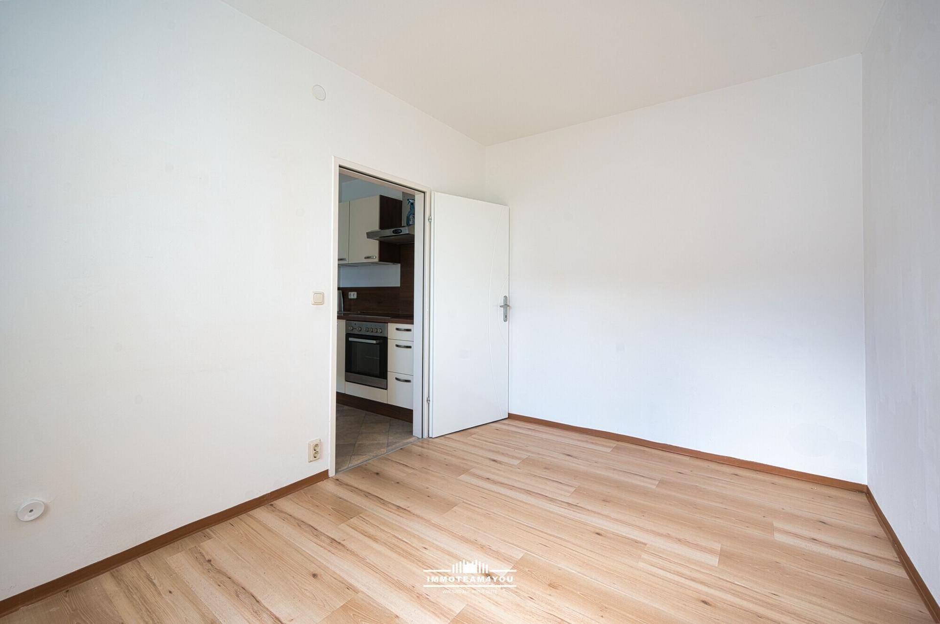 Leeres Zimmer mit Laminatboden und Tür zur Küche, bietet flexible Nutzungsmöglichkeiten.