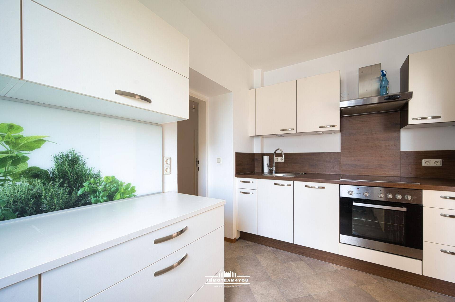 Moderne Einbauküche mit weißen Schränken, dunklen Arbeitsplatten und integriertem Backofen.