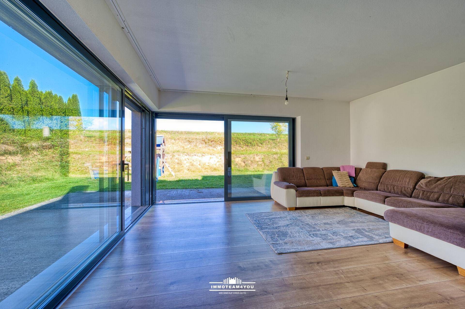 Helles Wohnzimmer mit großen Glasfronten, Holzboden und direktem Zugang zum Garten.