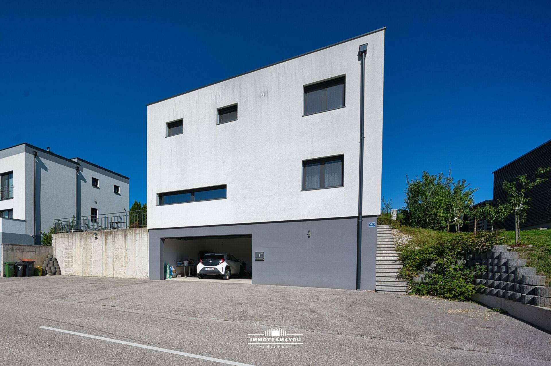 Moderne Hausfassade in Weiß und Grau mit integrierter Garage und Zufahrt.
