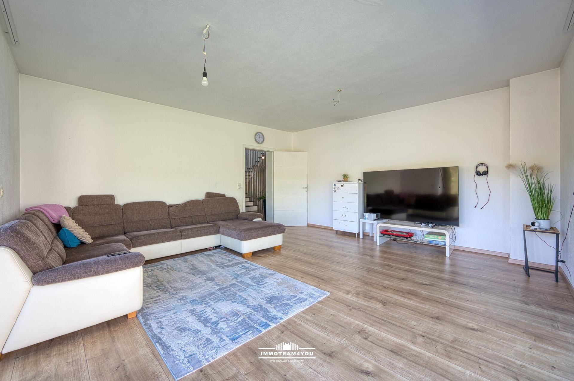 Geräumiges Wohnzimmer mit großem Sofa, Fernseher und hellem Holzboden.