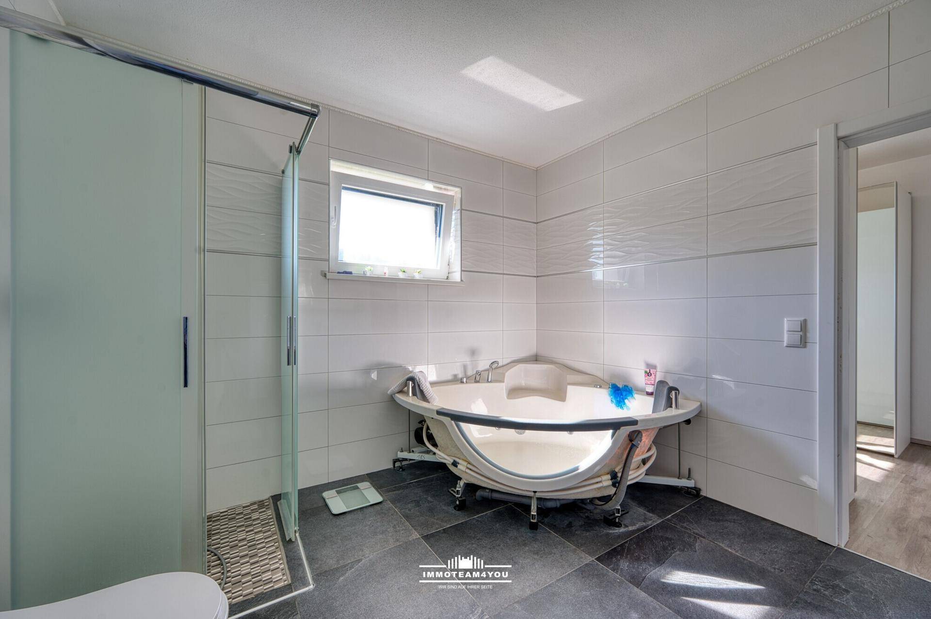 Modernes Badezimmer mit Eckbadewanne, Duschkabine und hellen Fliesen, mit Fenster.