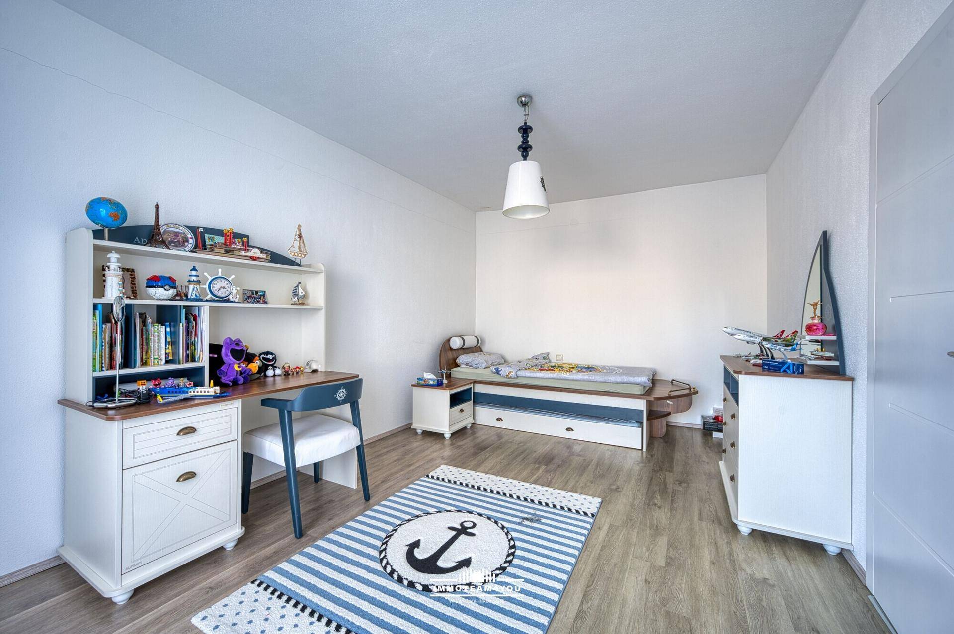 Kinderzimmer mit Schreibtisch, Regal und Bett, dekoriert mit maritimen Elementen, auf Holzboden.