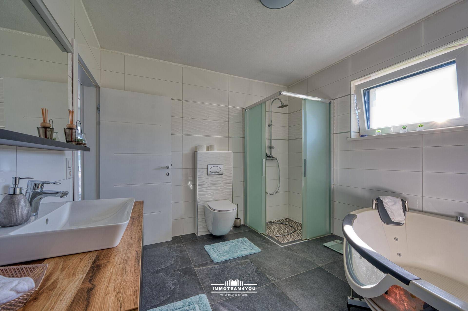 Helles Badezimmer mit Waschtisch, Toilette, Dusche und Eckbadewanne, mit Fenster.