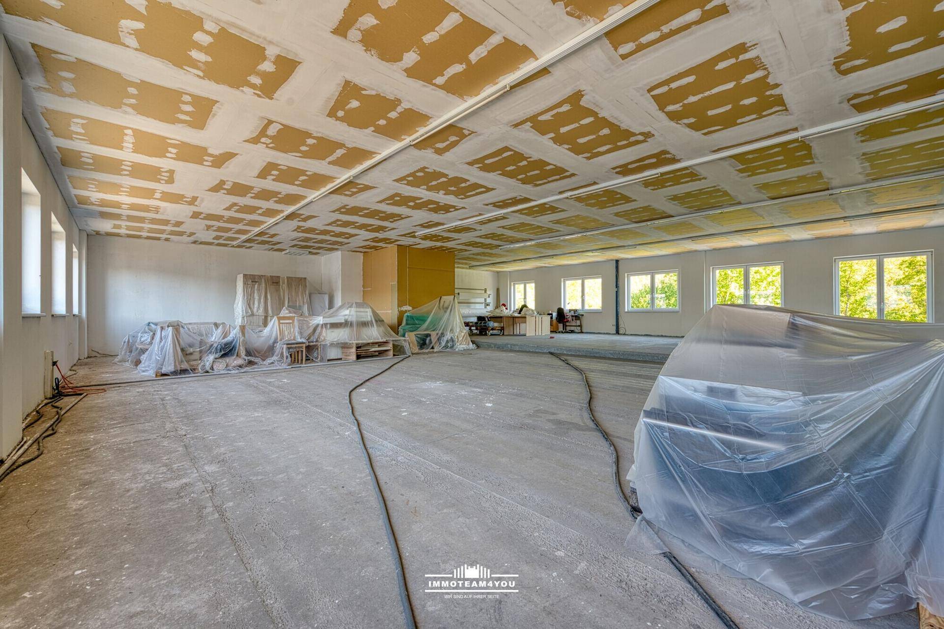 Großes Büro in Renovierung mit unfertiger Decke und viel Tageslicht.