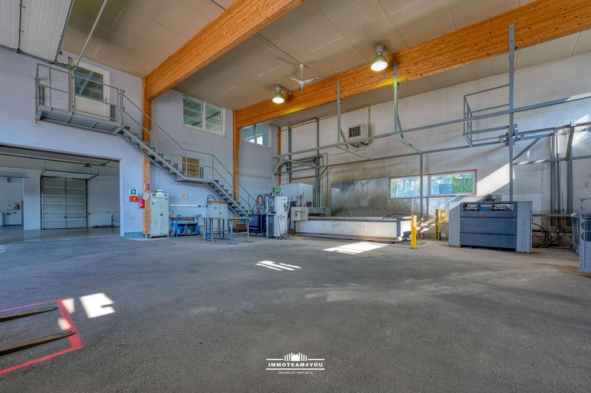 Große Lagerhalle mit Holzbalken, Betonboden und industrieller Beleuchtung.