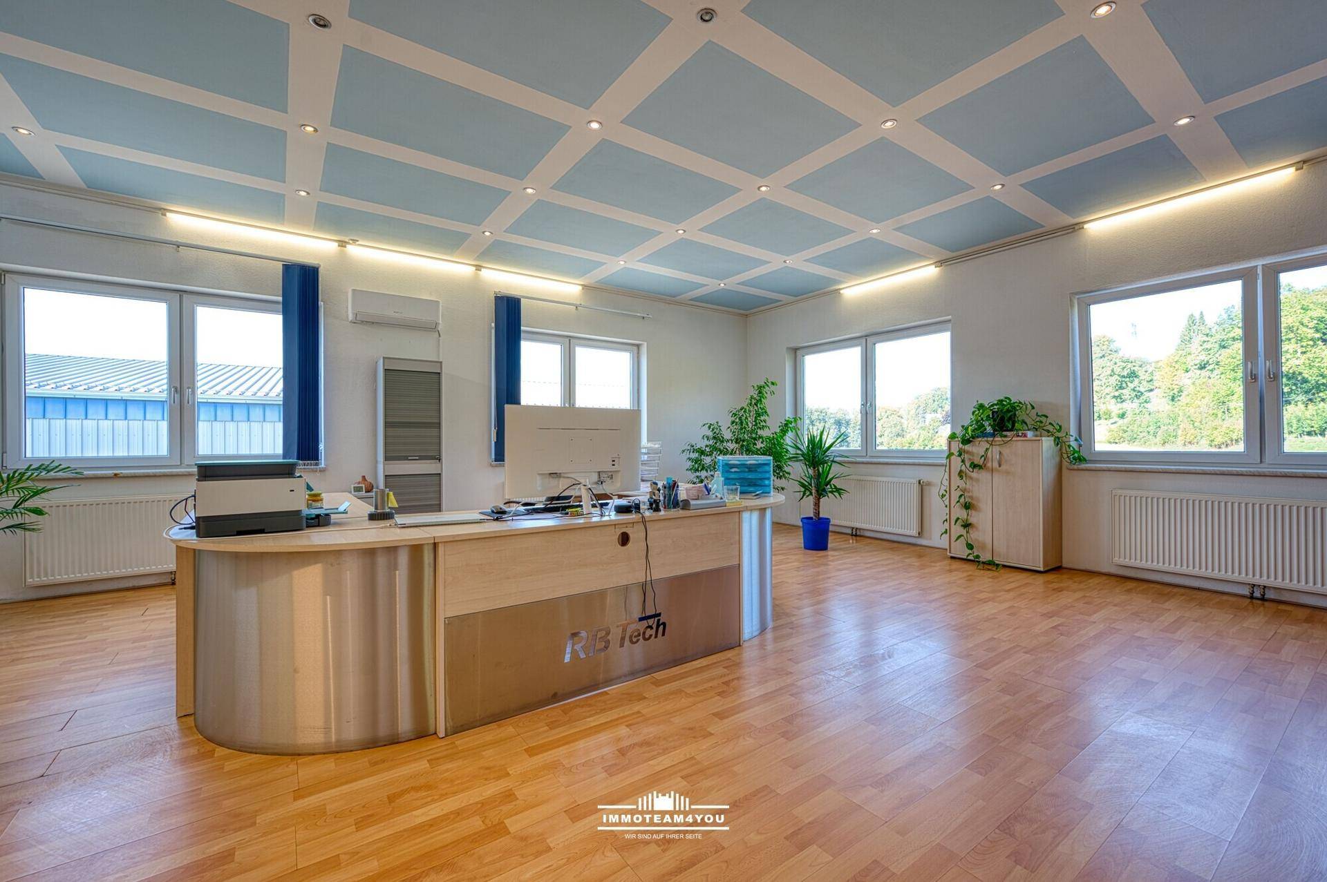 Großes Büro mit Holzboden, blauer Kassettendecke und vielen Fenstern für natürliches Licht.
