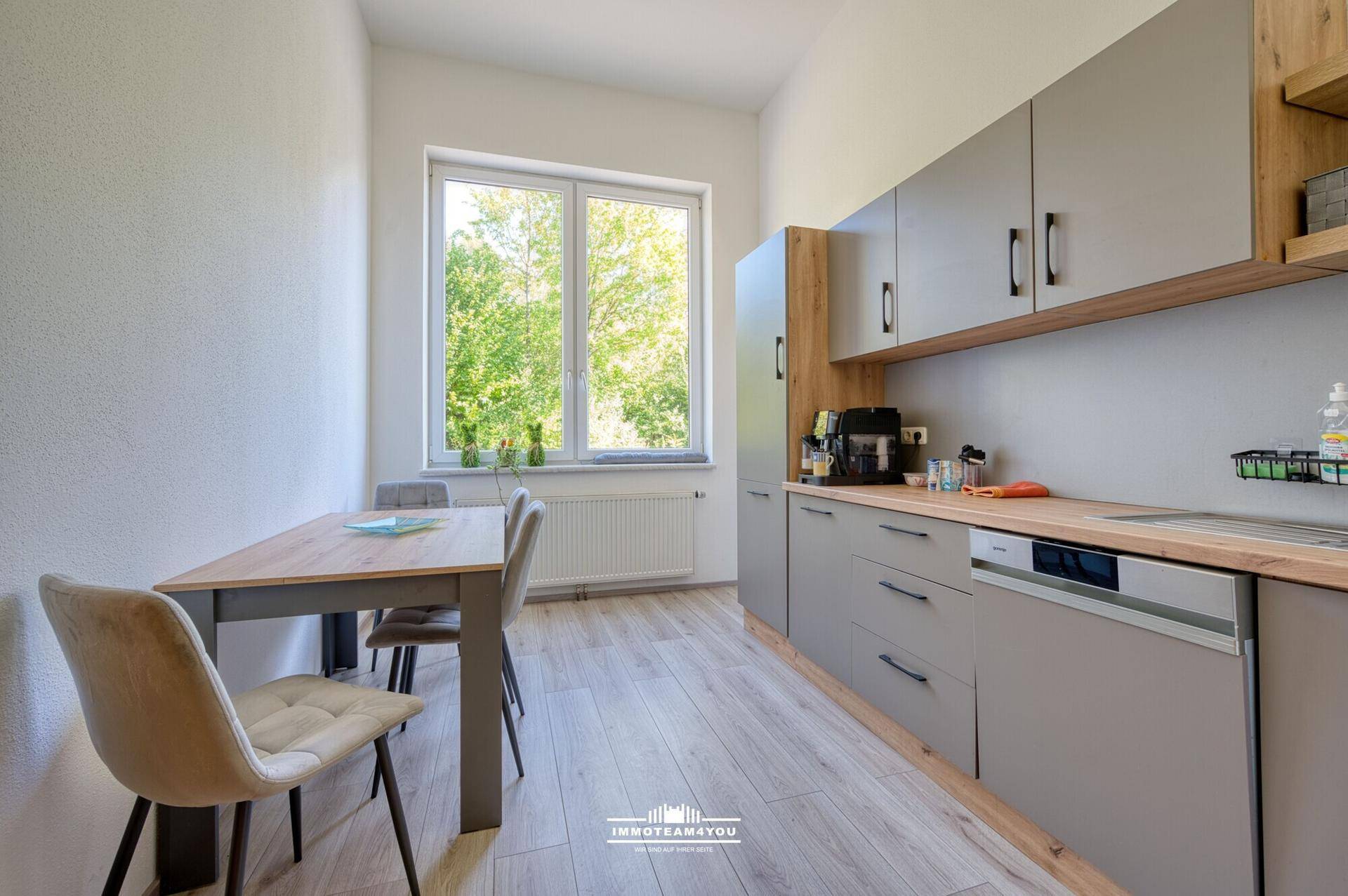 Moderne Küche mit grauen Schränken, Holzarbeitsplatte und Essbereich am Fenster.