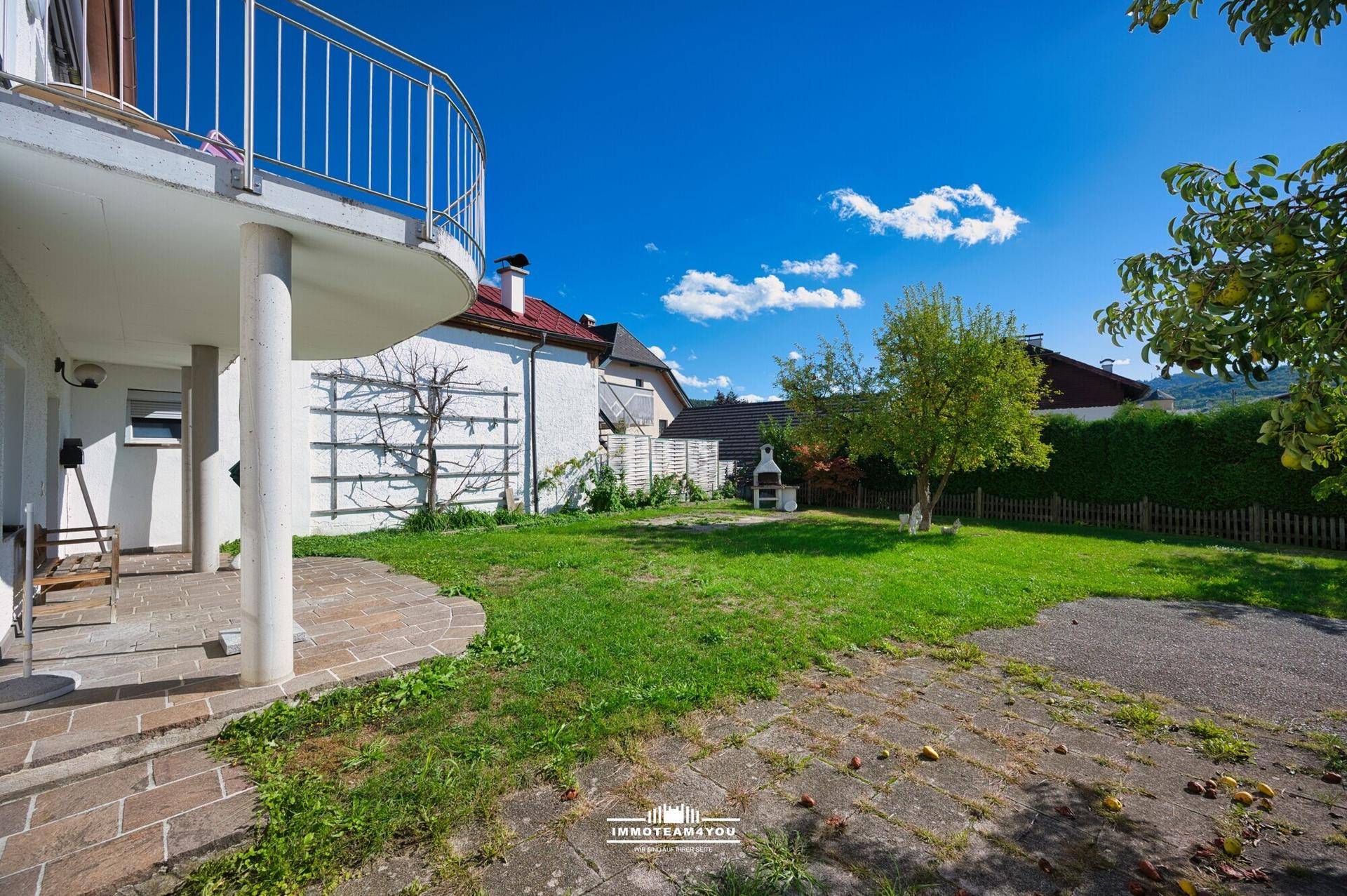 Grüner Gartenbereich mit Rasenfläche, Grillplatz und gepflastertem Sitzbereich.