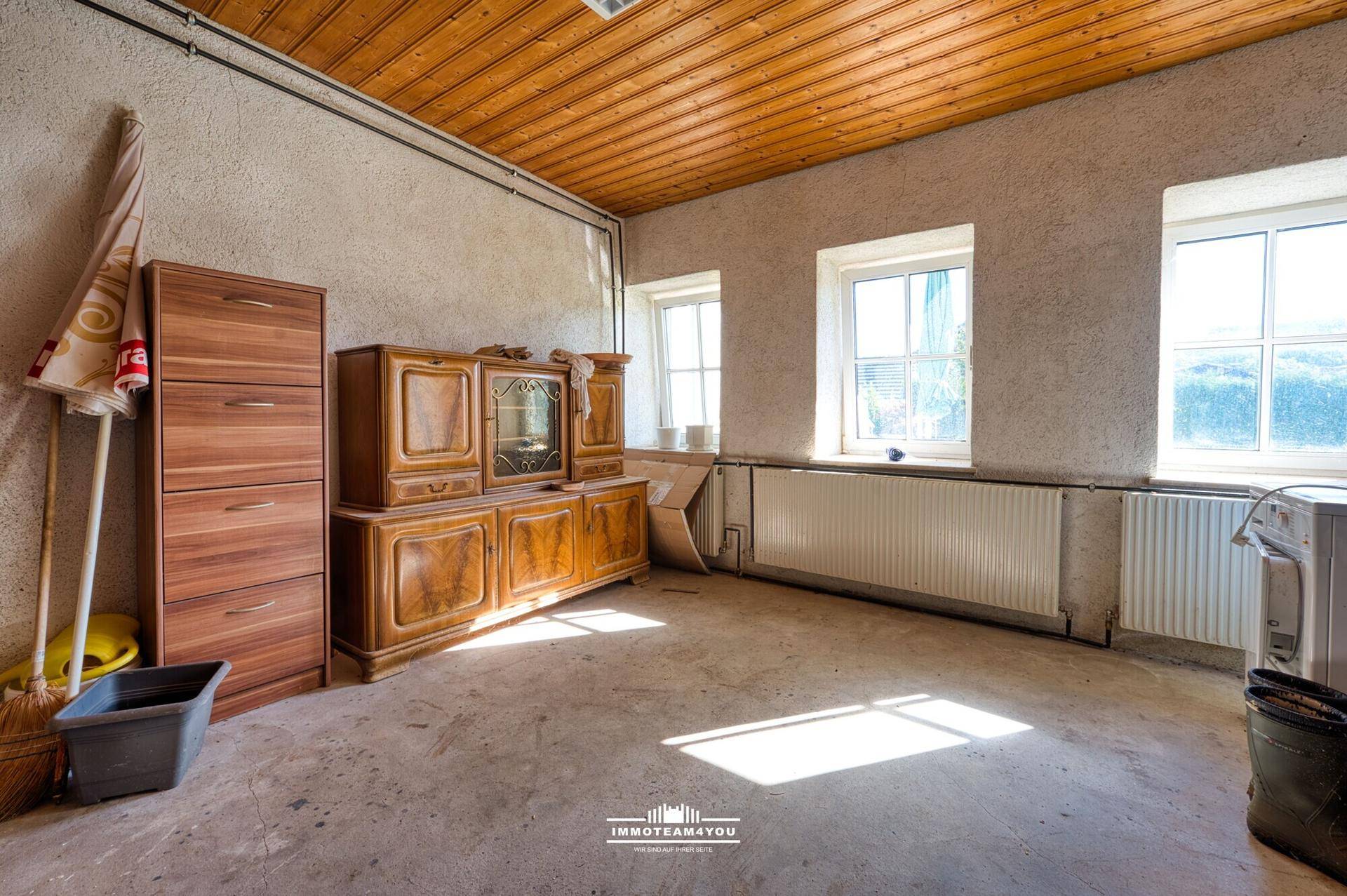 Geräumiger Raum mit Holzdecke, Betonboden und Fenstern.