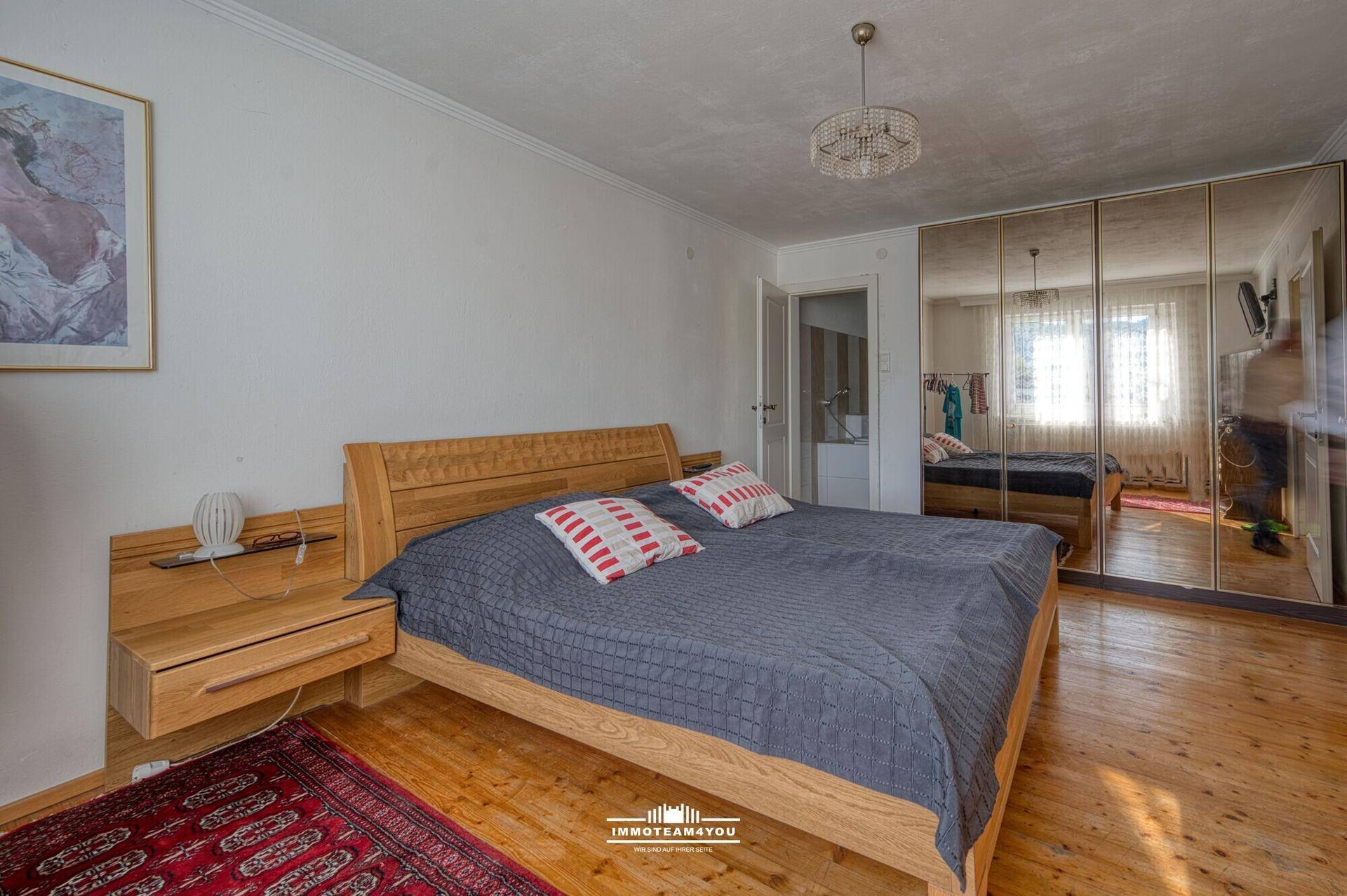 Schlafzimmer mit Holzbett, Spiegelschränken und Holzdielenboden.