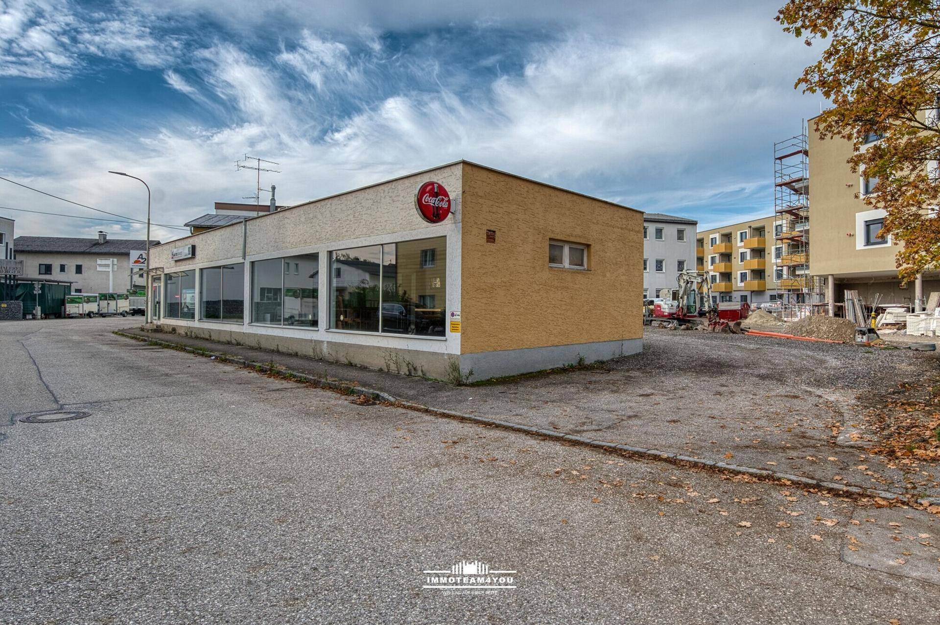 Gebäudeansicht mit Parkplatz und Baustelle im Hintergrund unter bewölktem Himmel.