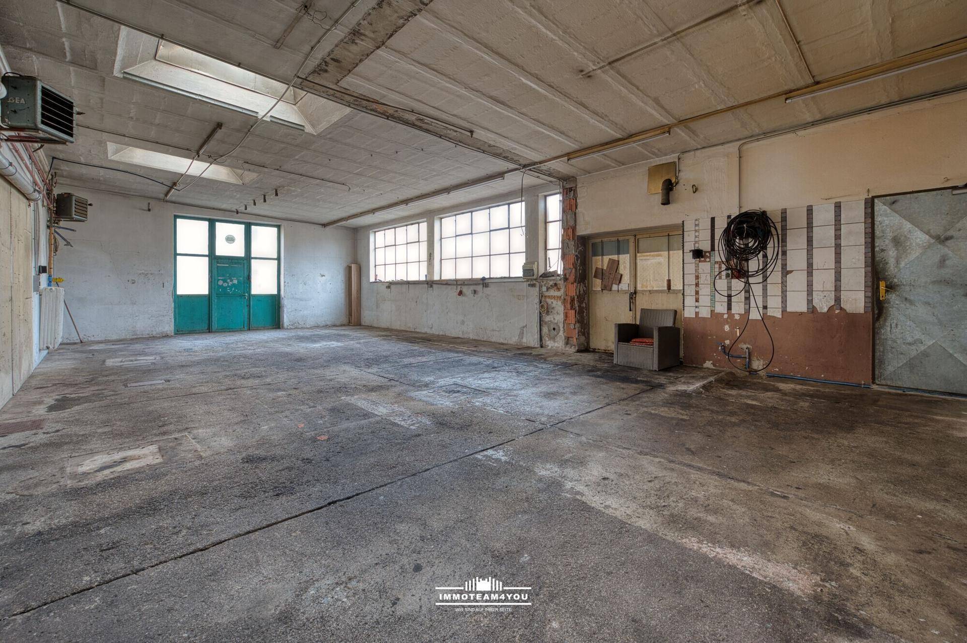 Geräumige Werkstatt mit großen Fenstern, Betonboden und viel Tageslicht, ideal für Handwerk.