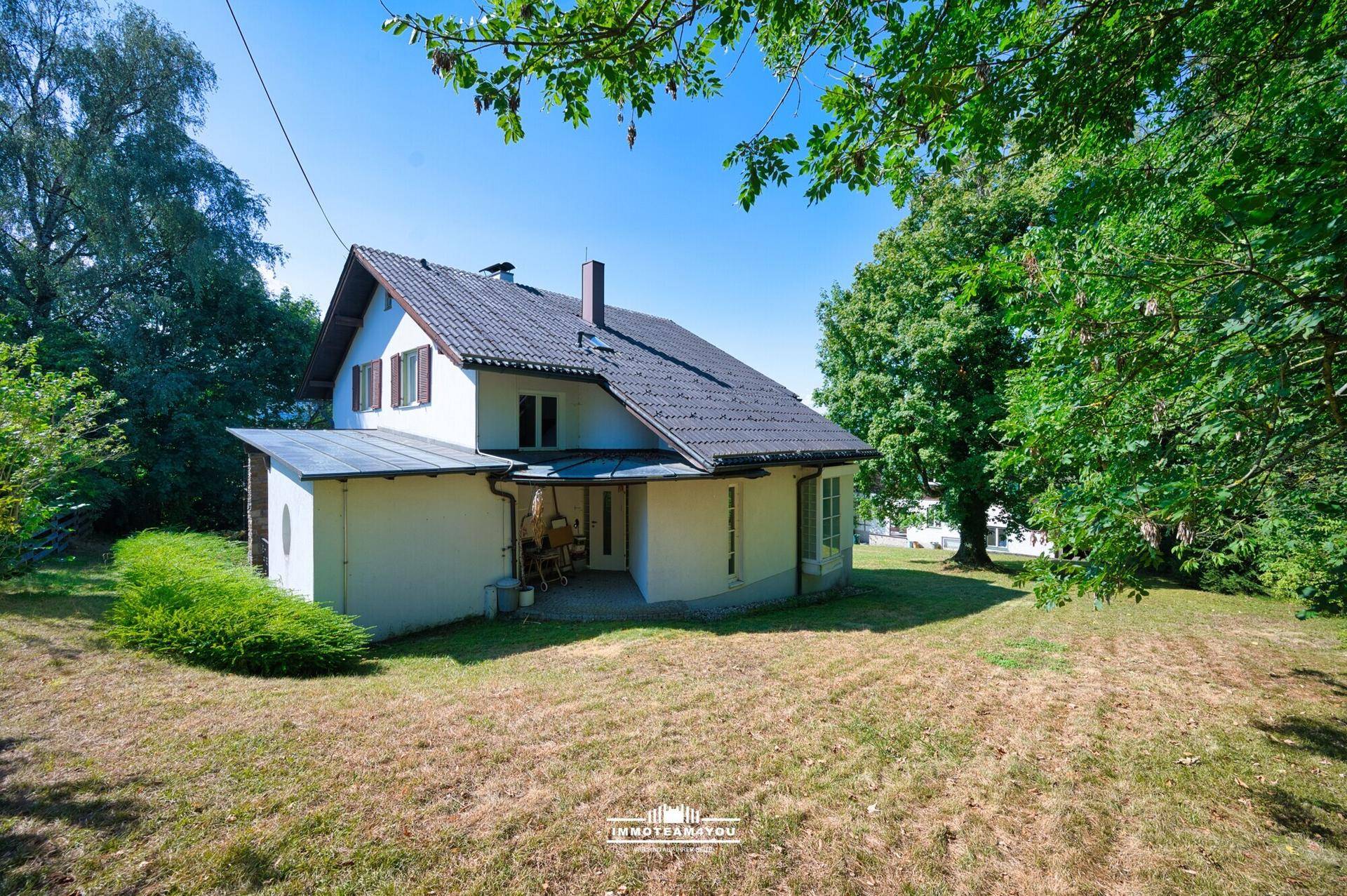 Seitenansicht des Hauses mit großem Gartenbereich und altem Baumbestand unter strahlendem Himmel.