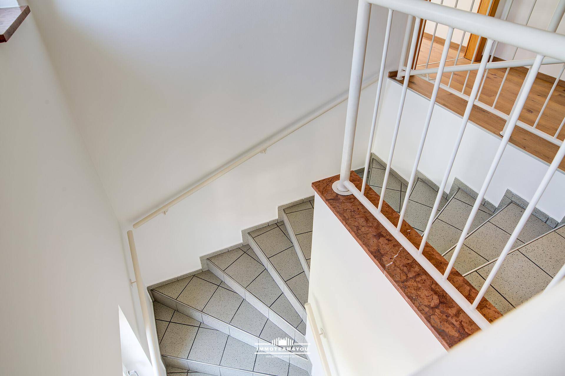 Treppenhaus mit gefliesten Stufen, weißem Geländer und Marmorakzenten.