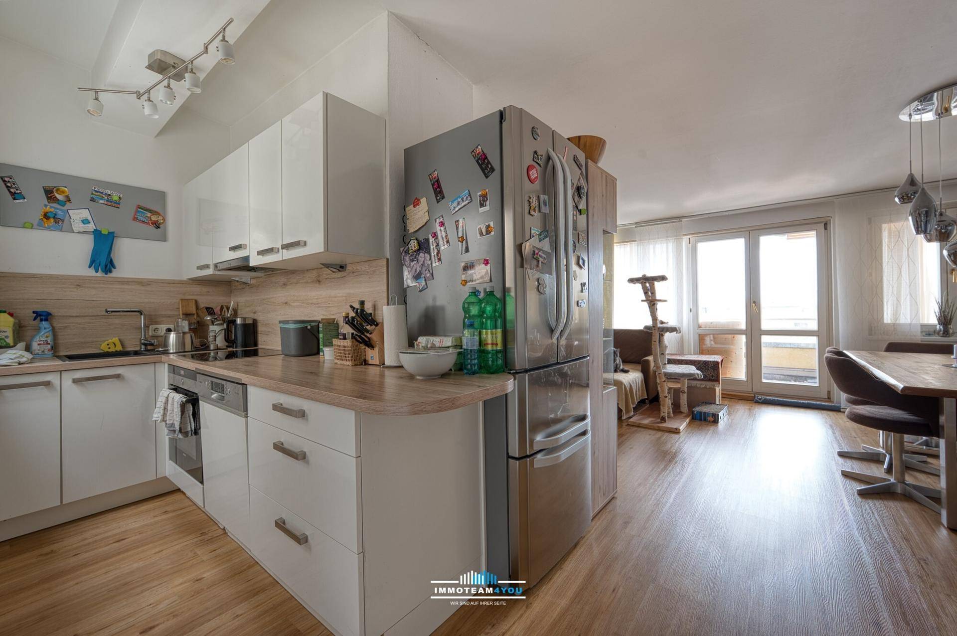 Offener Wohn- und Essbereich mit moderner Küche, Holzboden und Zugang zum Balkon.