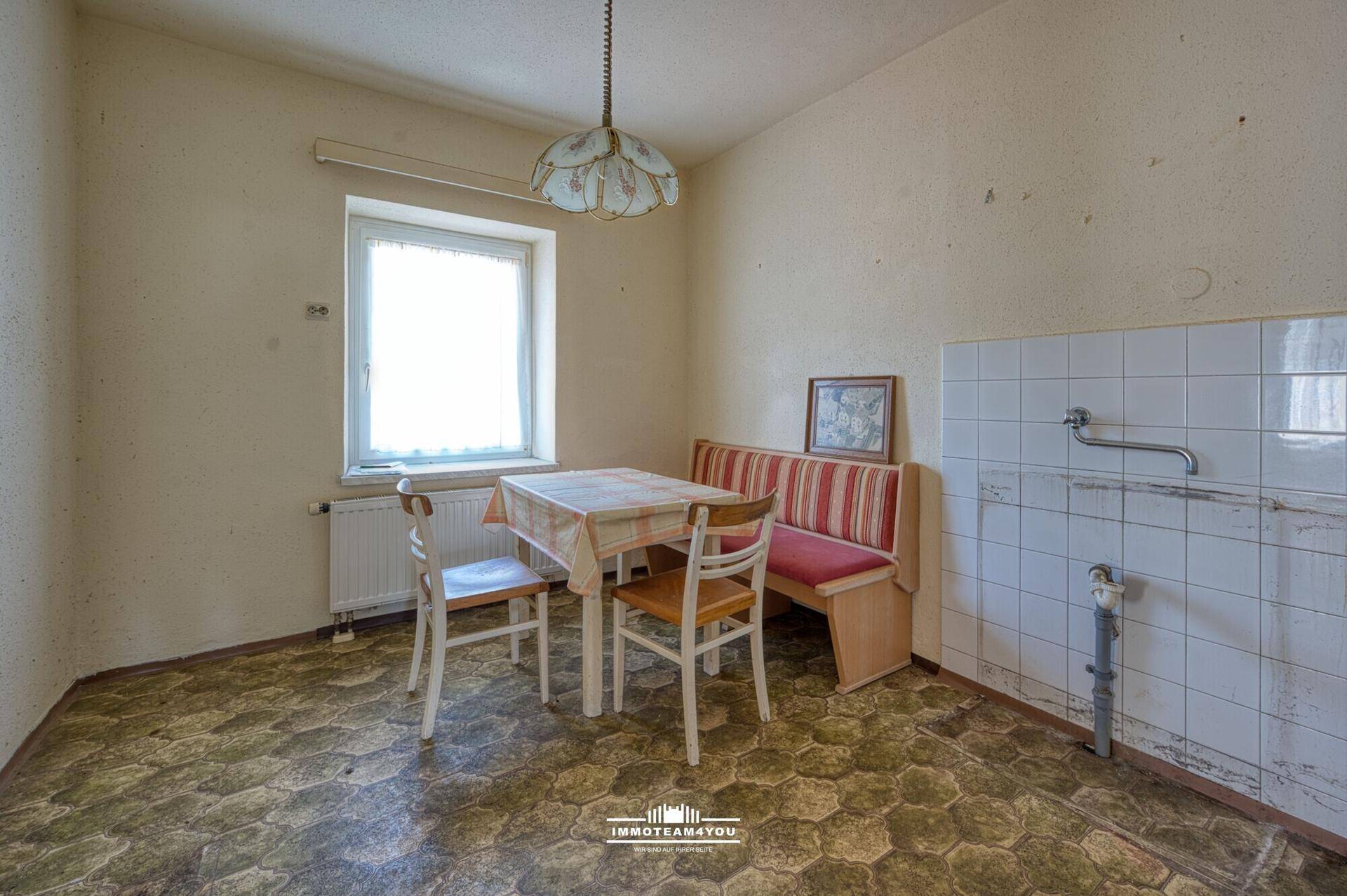 Einfache Küche mit Essbereich, Fenster und älteren Fliesen, renovierungsbedürftig.