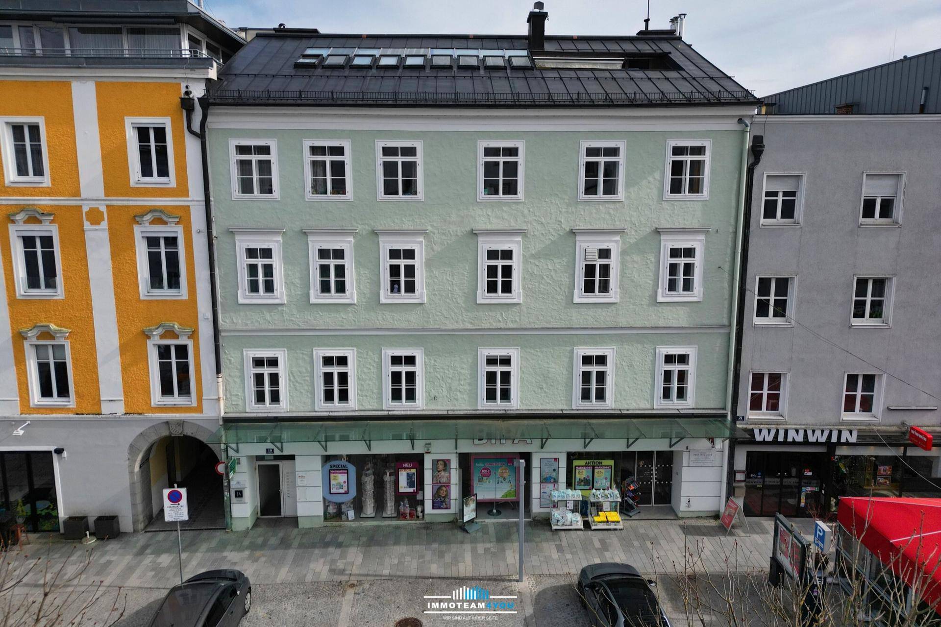 Frontansicht eines historischen Gebäudes mit hellgrüner Fassade und Dachfenstern in der obersten Etage.