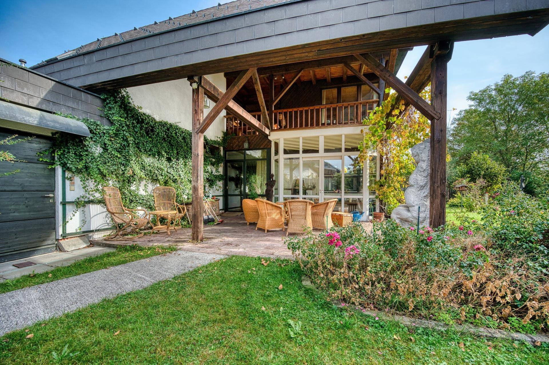 Überdachte Terrasse mit Korbmöbeln und üppiger Begrünung, ideal für entspannte Stunden im Freien.