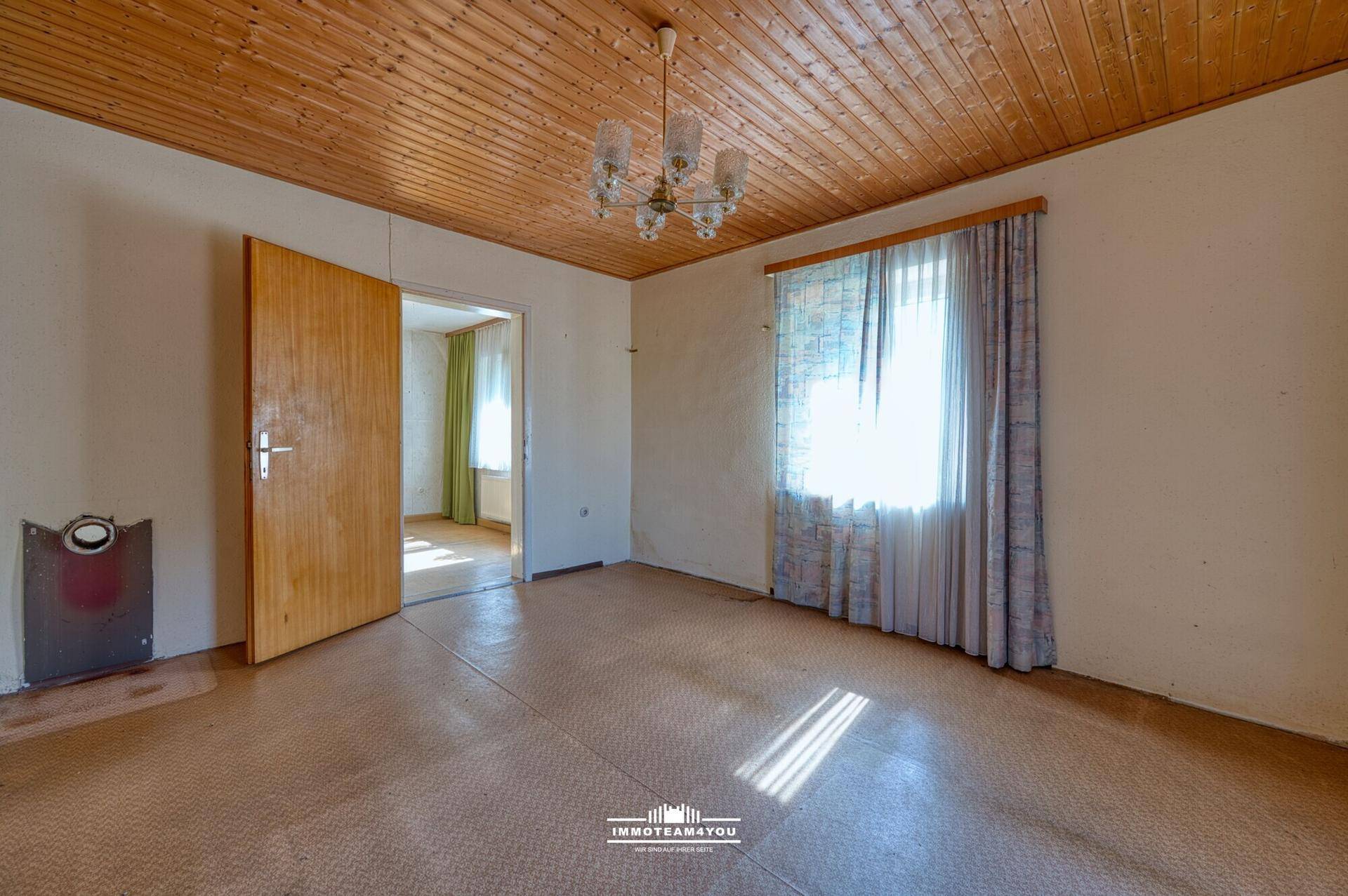 Geräumiger Raum mit Holztäfeldecke, älterem Bodenbelag und Fenster, renovierungsbedürftig.