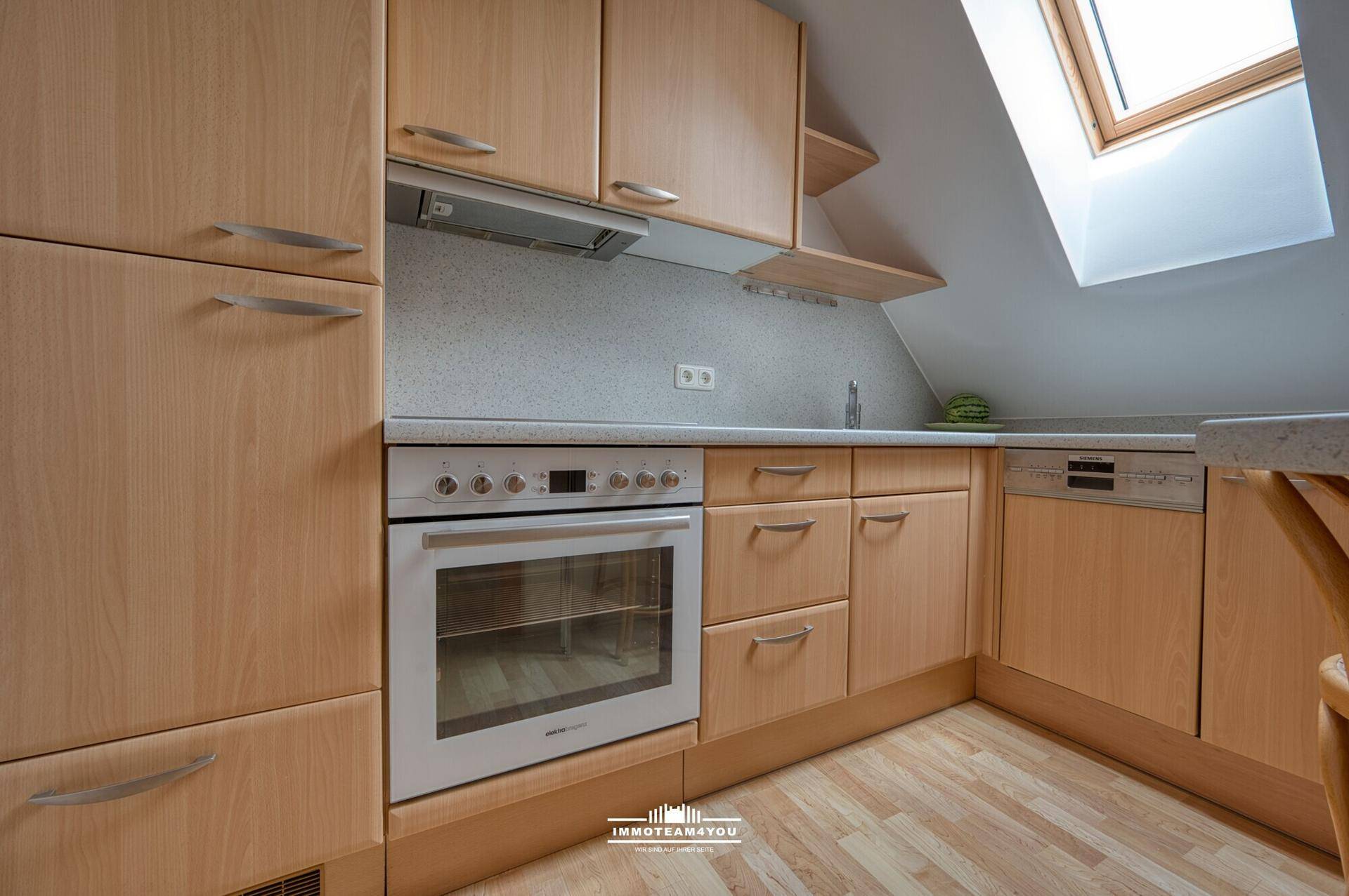 Kleine Küche im Dachgeschoss mit Holzschränken, Einbaugeräten und Dachfenster.