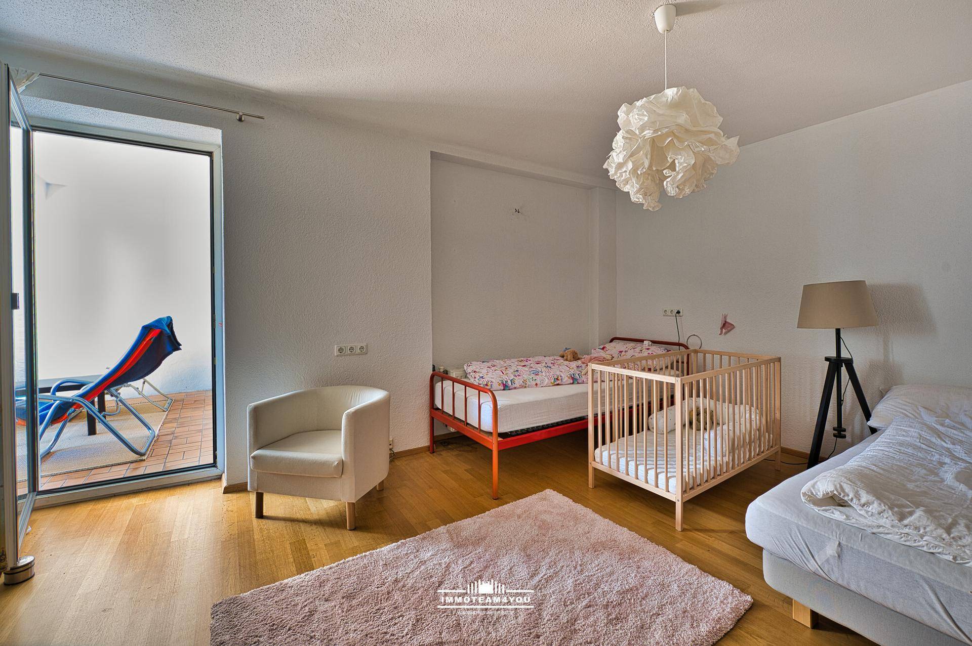 Kinderzimmer mit Holzboden, Babybett und Zugang zu einem kleinen Balkon.