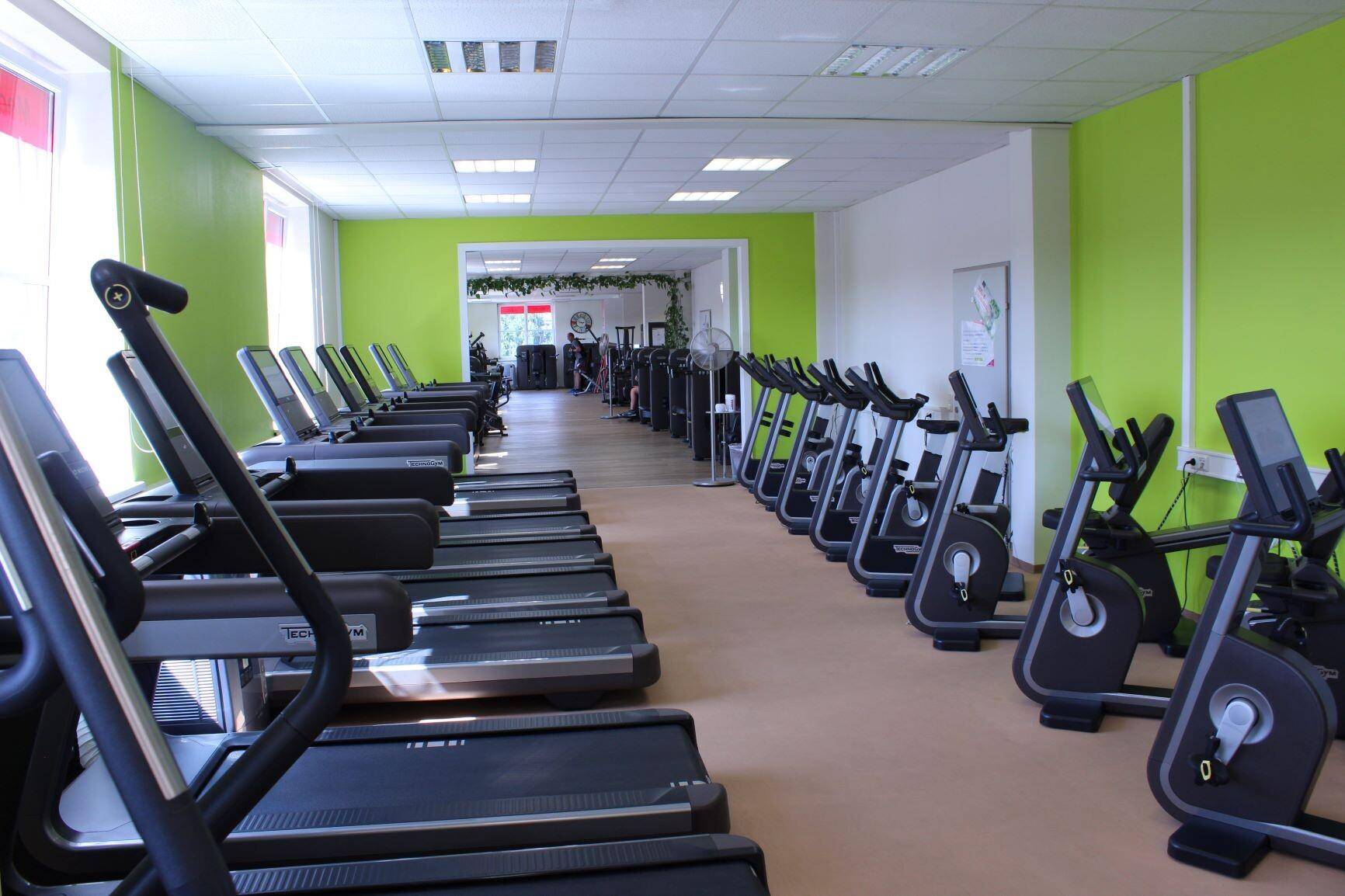Geräumiger Fitnessraum mit einer Reihe von Laufbändern und Crosstrainern, bereit für das Training.