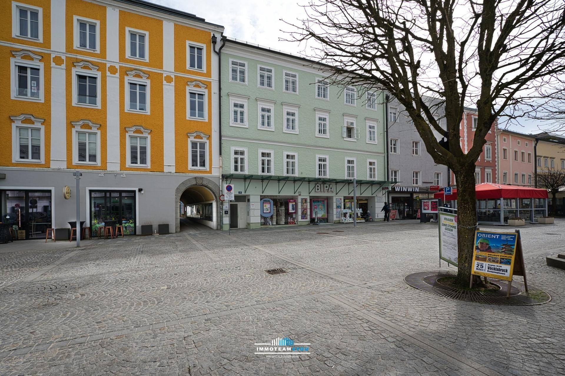 Kopfsteinpflasterstraße in einer historischen Stadt mit Gebäuden und einem Baum im Vordergrund.
