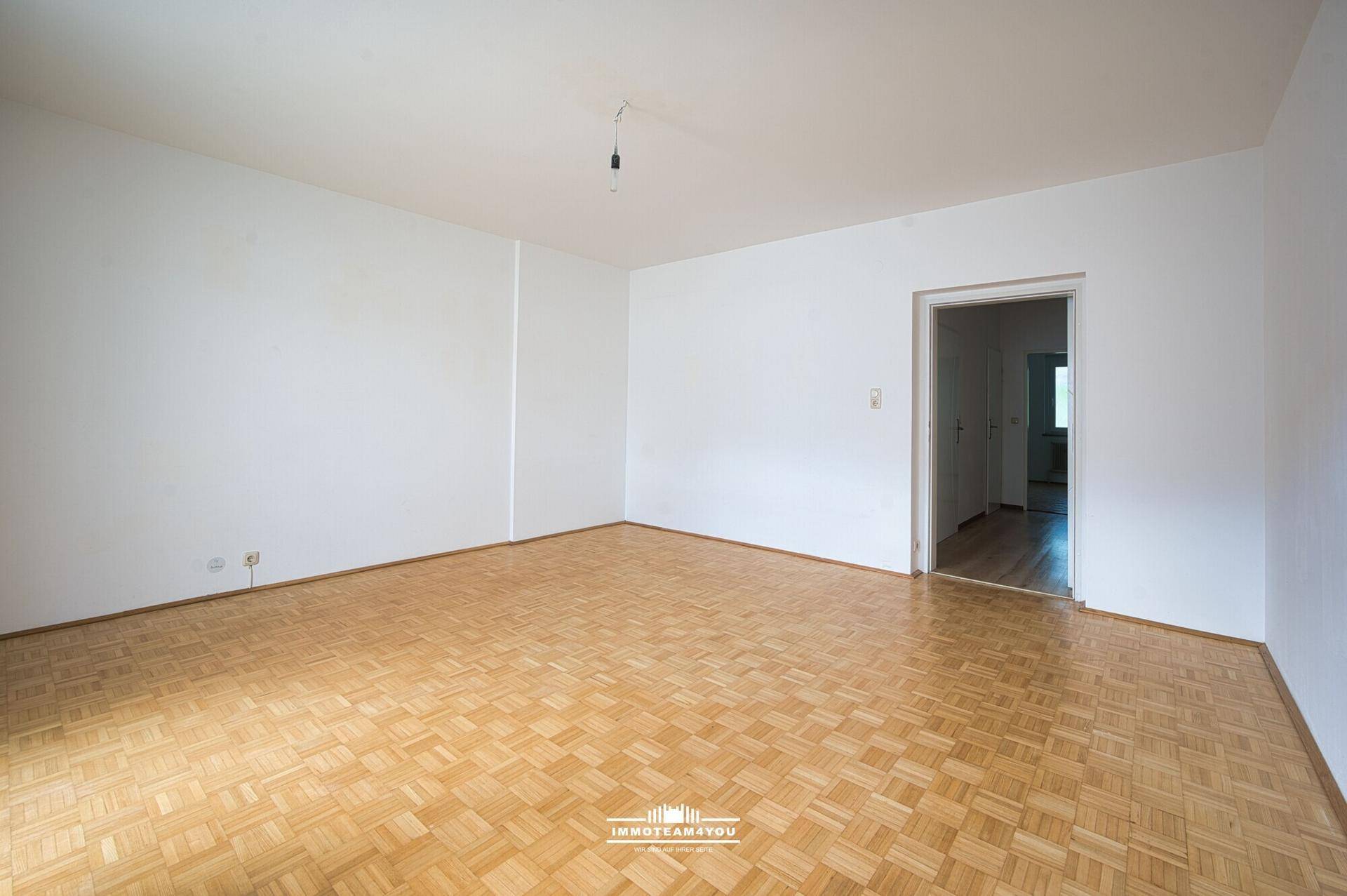 Leeres Zimmer mit klassischem Parkettboden und weiß gestrichenen Wänden, bereit zur individuellen Gestaltung.