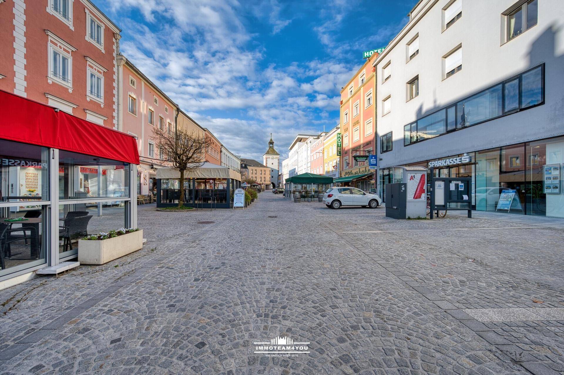 Historische Stadtstraße mit Kopfsteinpflaster, Geschäften und Restaurants unter blauem Himmel.