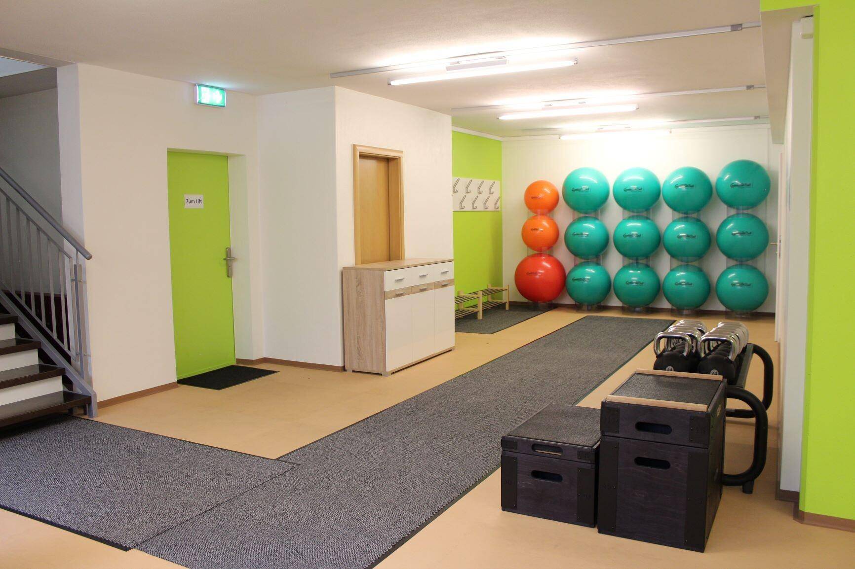 Eingangsbereich zum Fitnessbereich mit Treppe, Spinden und Gymnastikbällen, hell und funktional.