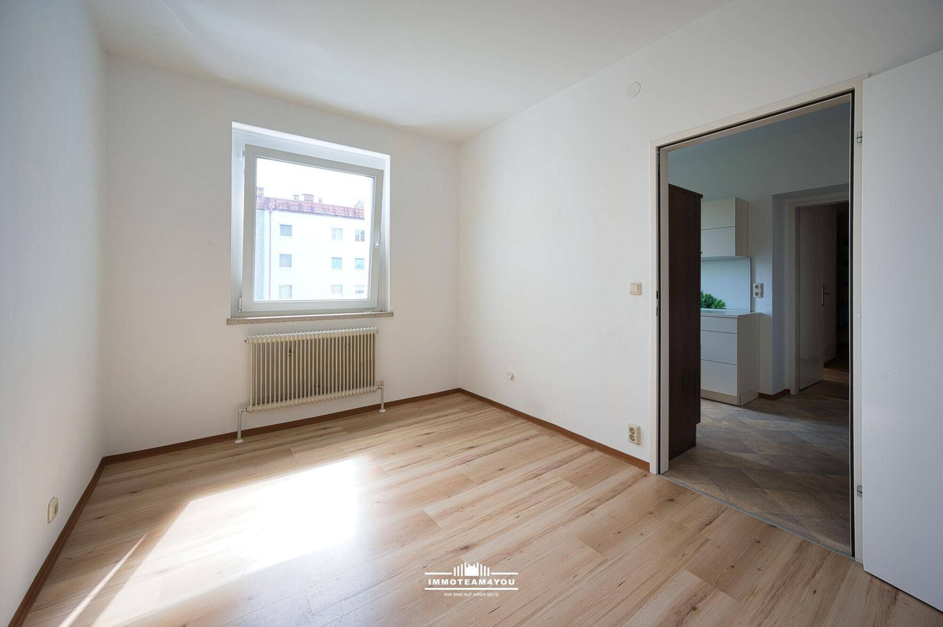 Helles Zimmer mit hellem Holzfußboden und Fenster, das einen Blick nach draußen bietet.