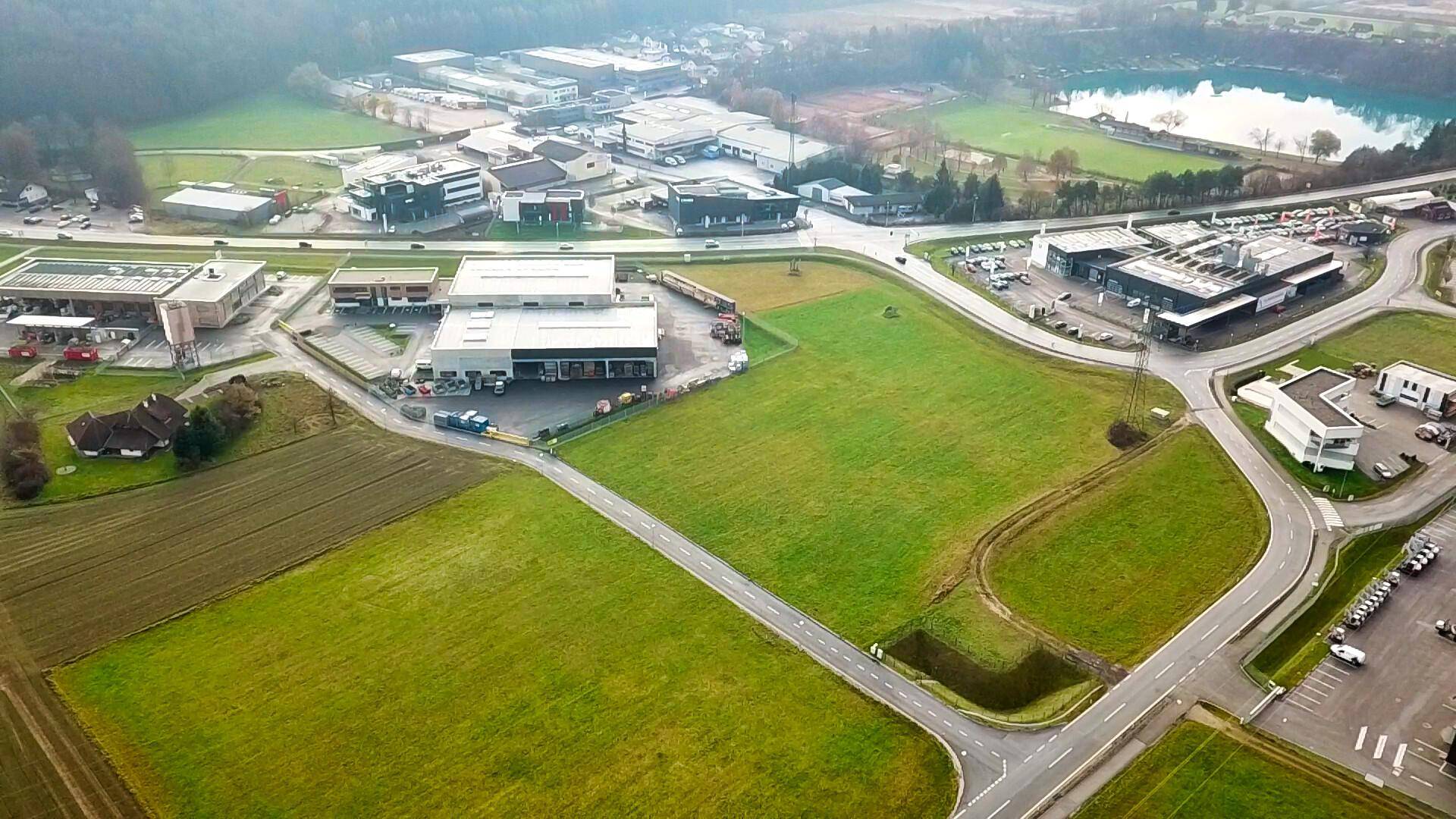 Panoramische Luftaufnahme eines großen Grundstücks mit angrenzenden Straßen, Gewerbegebäuden und einem See im Hintergrund.